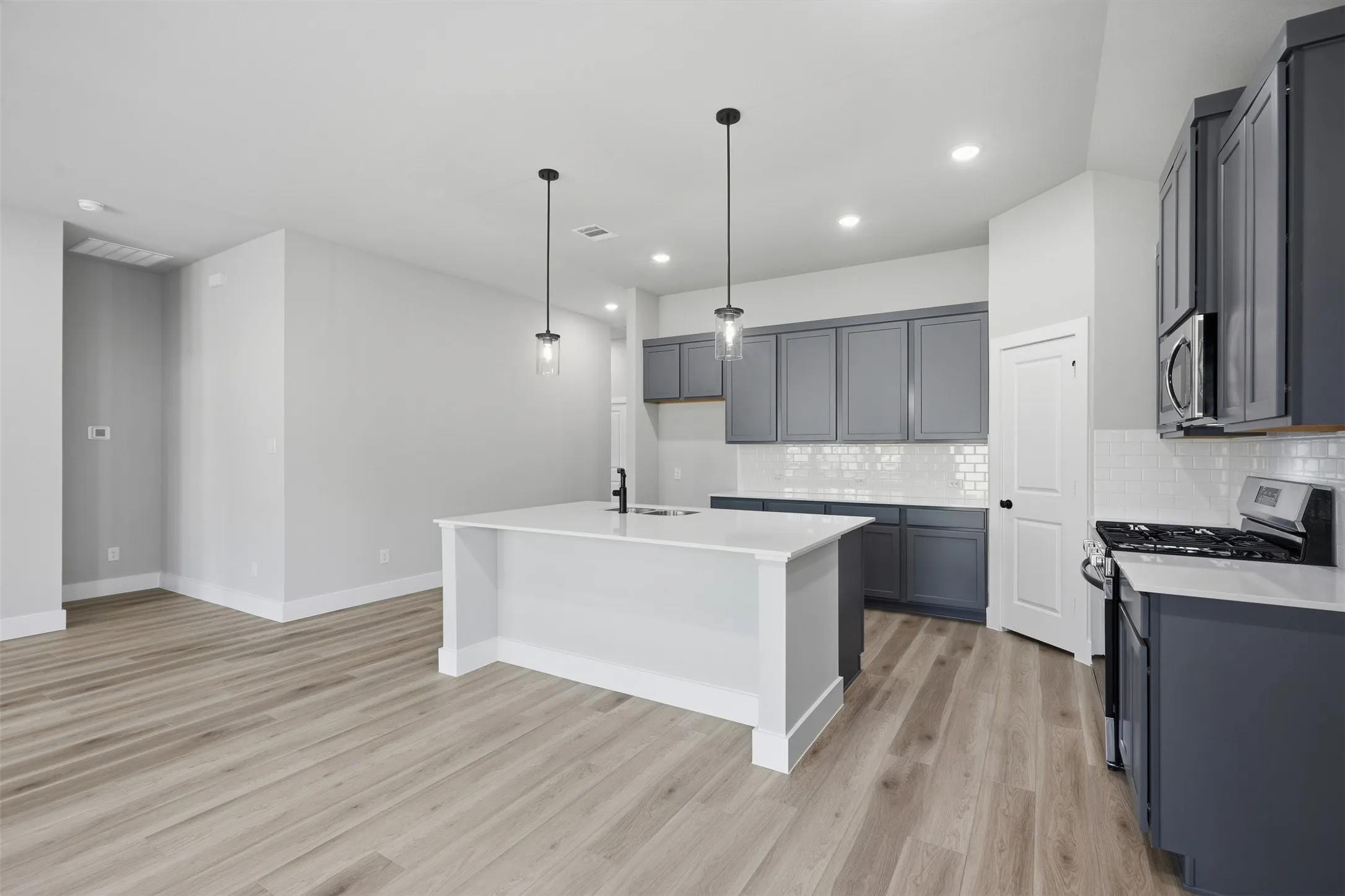 Modern kitchen featuring slate-toned cabinetry, white subway tile backsplash, and a central island with a sink