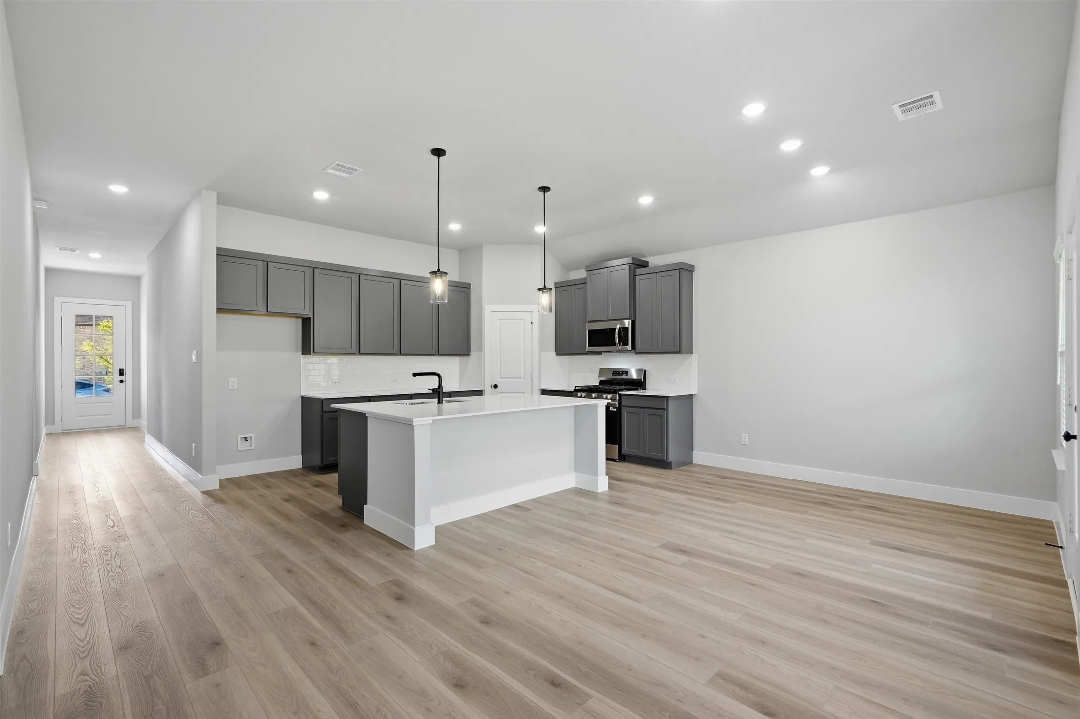Open-concept layout featuring wood-finish flooring, recessed lighting, and a kitchen island with pendant lighting