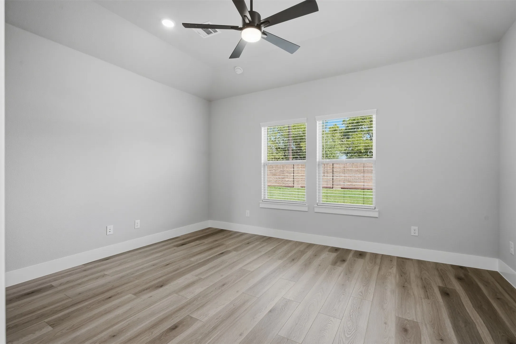 Wood-finish flooring, dual windows with blinds, ceiling fan, recessed lighting, and crisp white trim