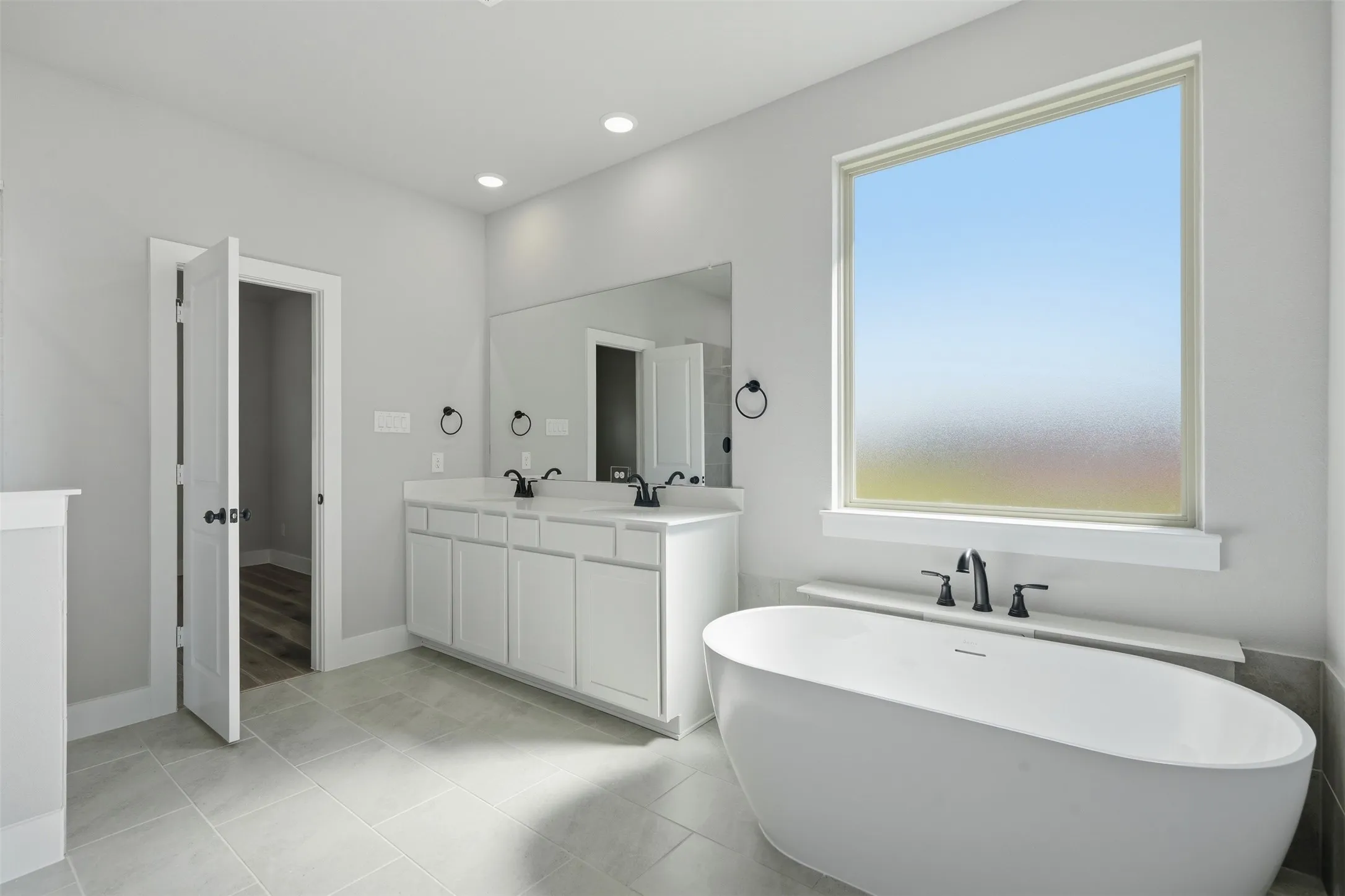 Spacious bathroom featuring a freestanding soaking tub, dual vanity with undermount sinks, large mirror, and tile flooring