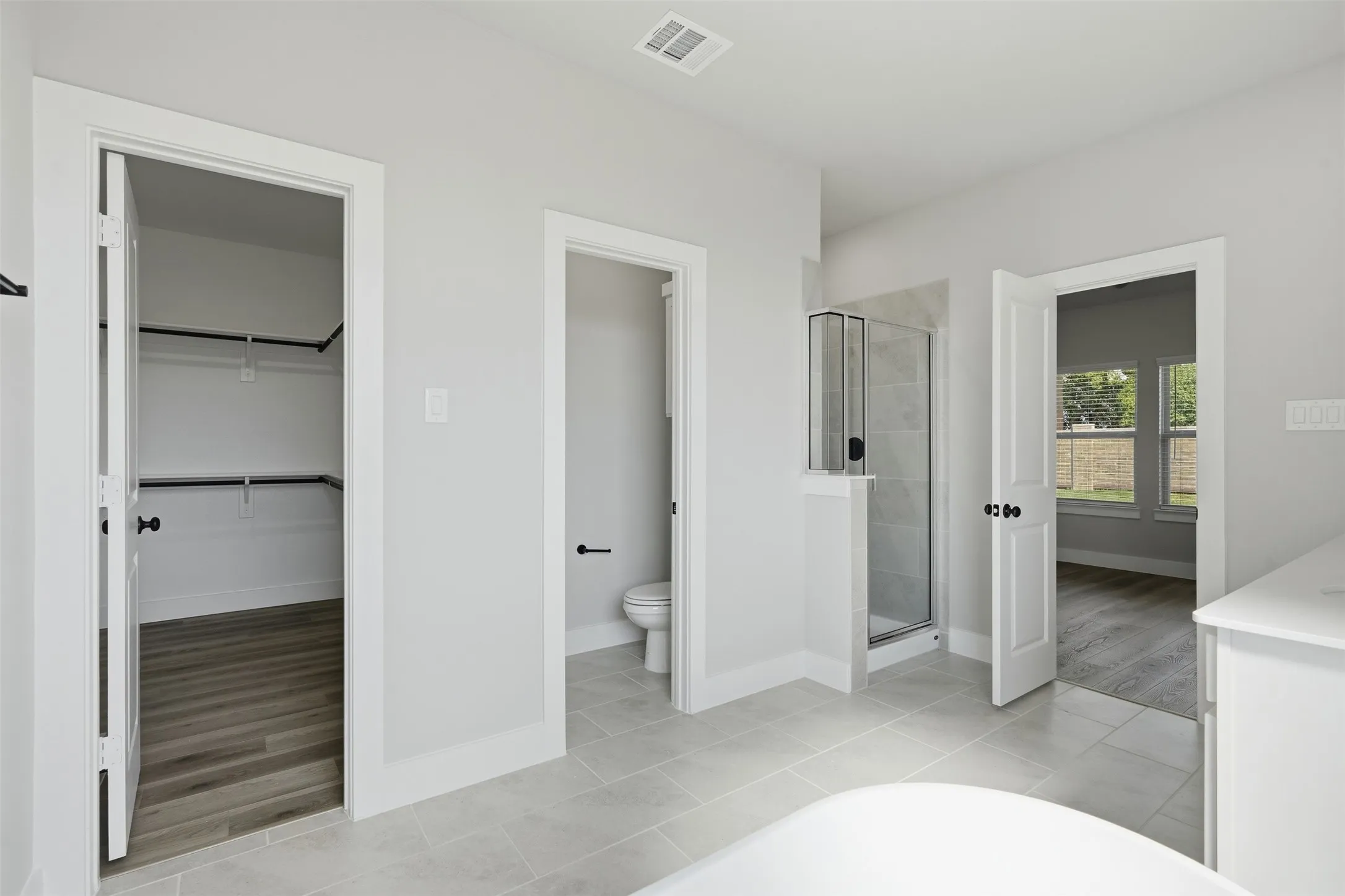 Light gray tile flooring, walk-in shower with glass enclosure, separate water closet, walk-in closet with built-in shelving, wood-finish flooring in adjacent room
