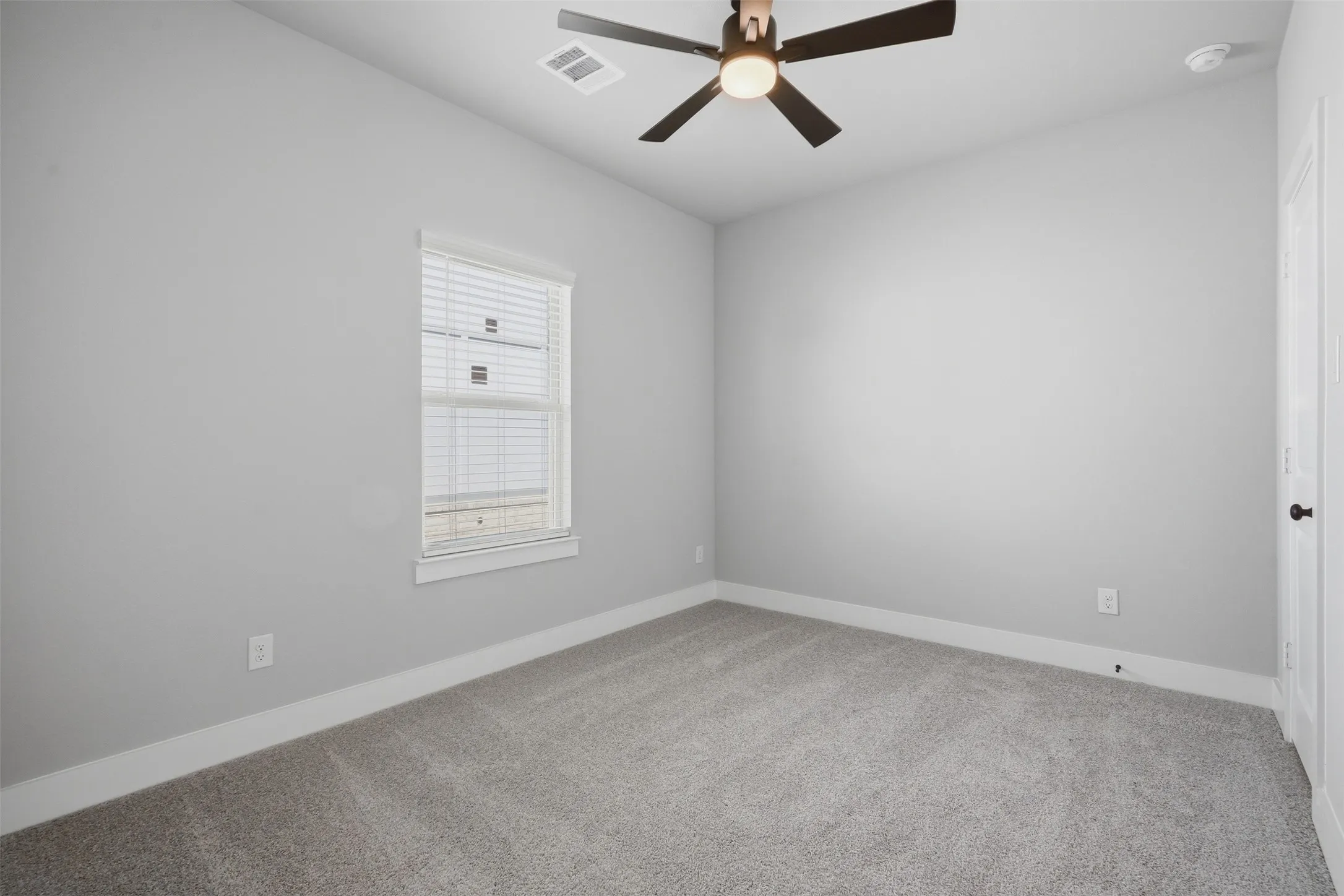 Neutral wall paint, carpet flooring, window with blinds, ceiling fan with integrated lighting, and white trim throughout