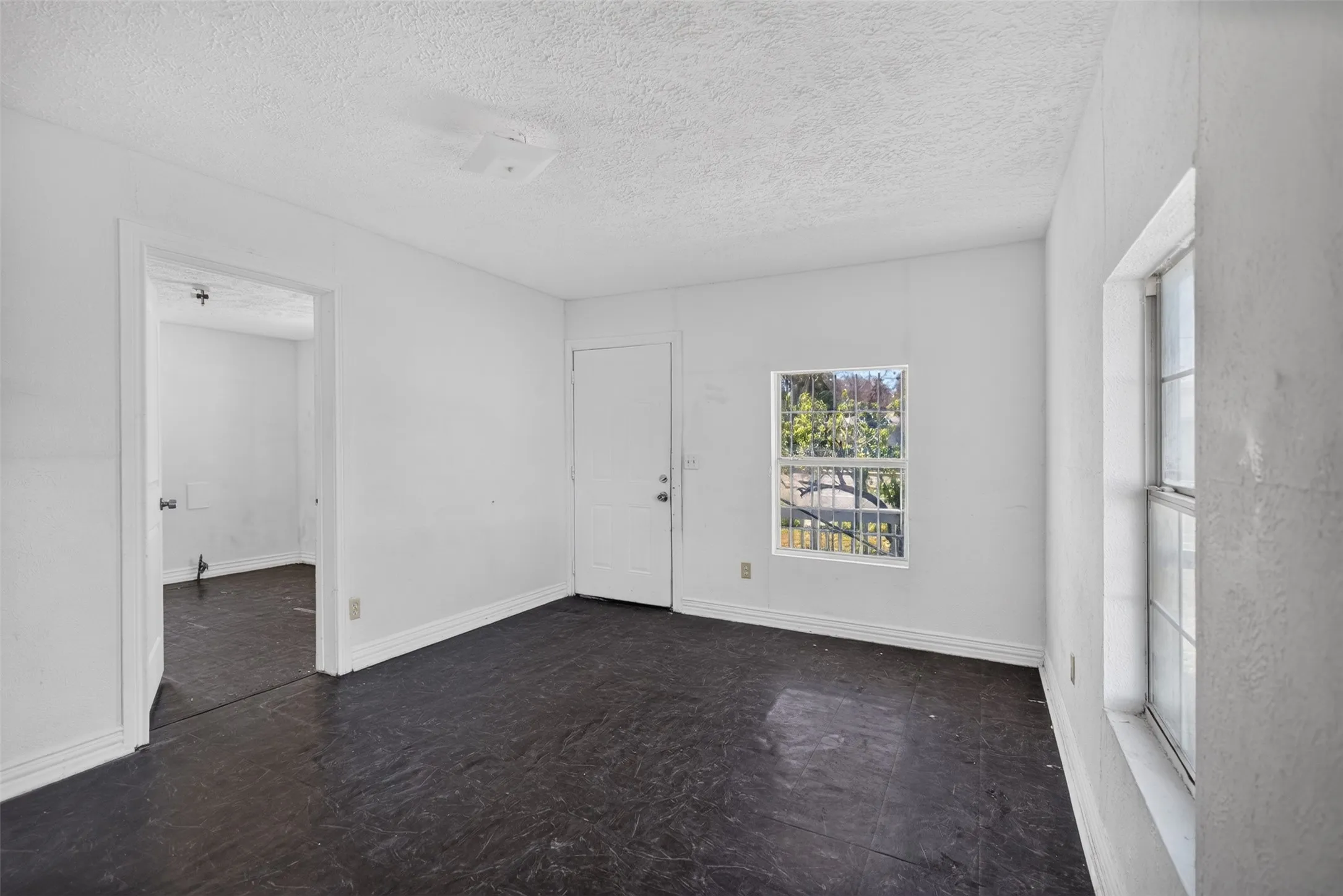 White painted walls, dark flooring, multiple windows, and a solid entry door