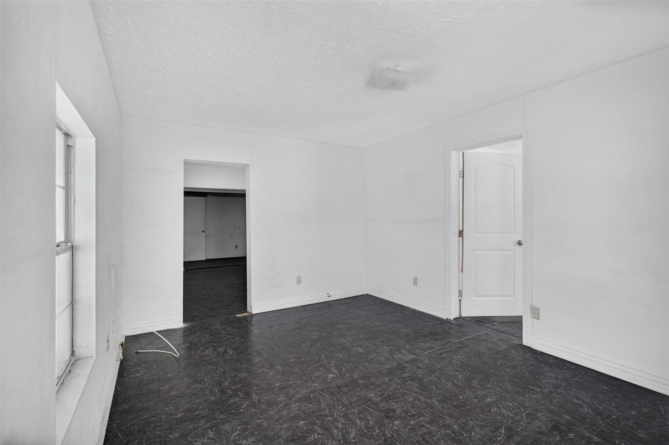 White painted walls, dark flooring, and a window providing natural illumination