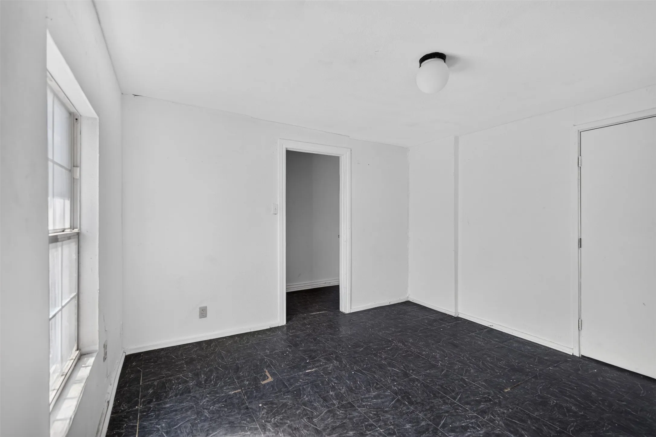 White walls, dark flooring, window with grid panes, flush mount ceiling light, interior doors
