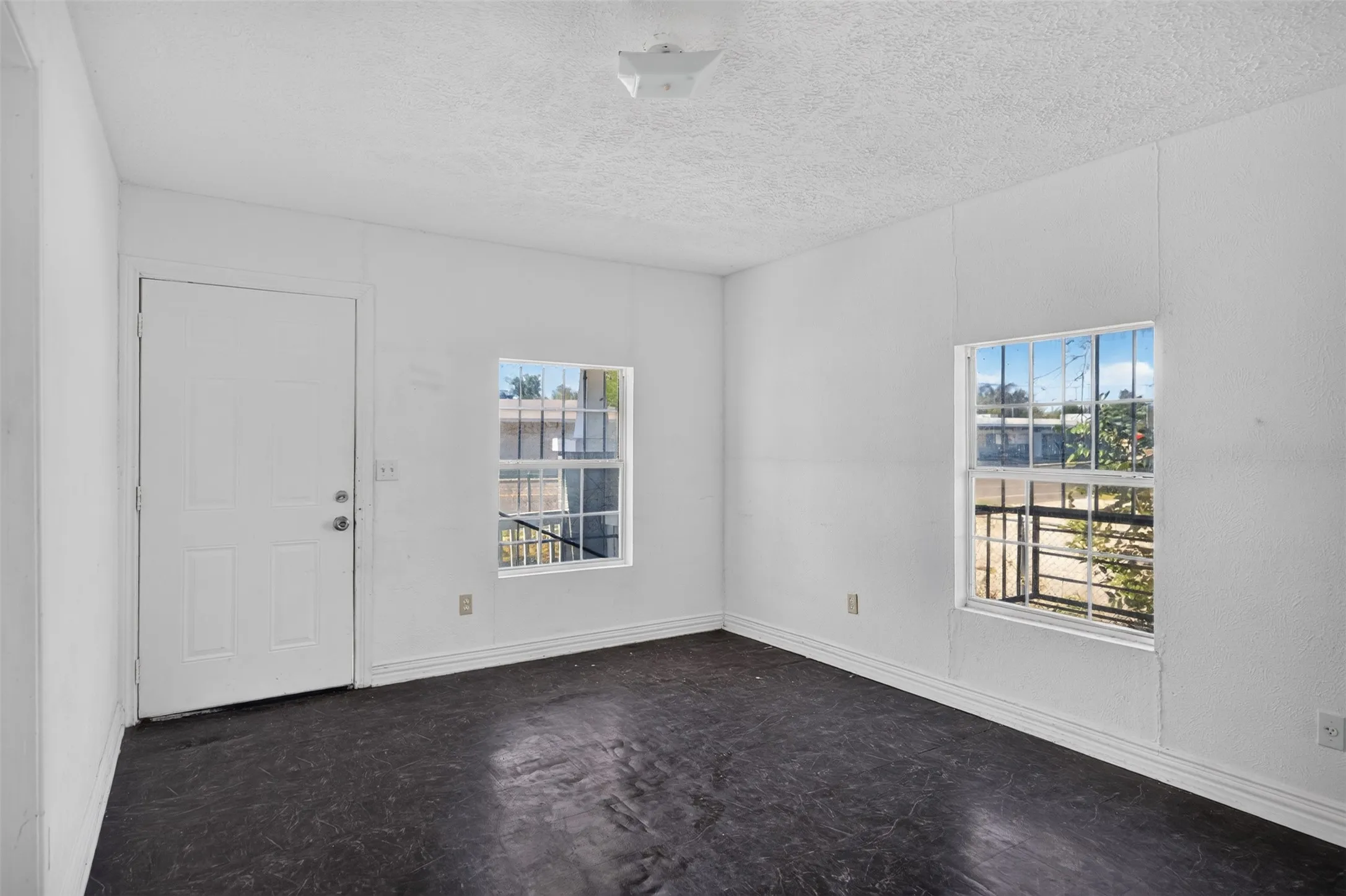 White interior walls with baseboard trim, dual windows with security bars, and a white panel door