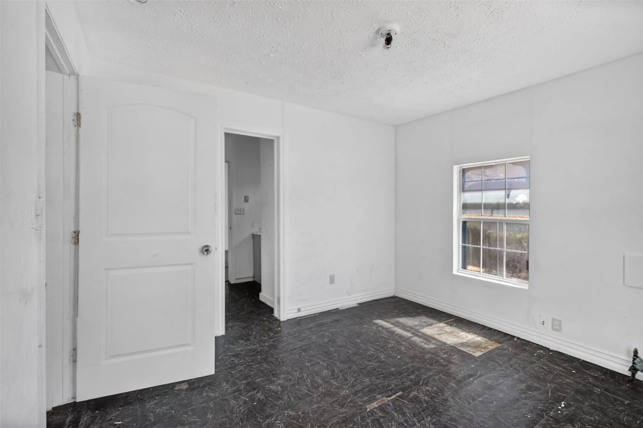 Room featuring dark flooring, white walls, and a single pane window