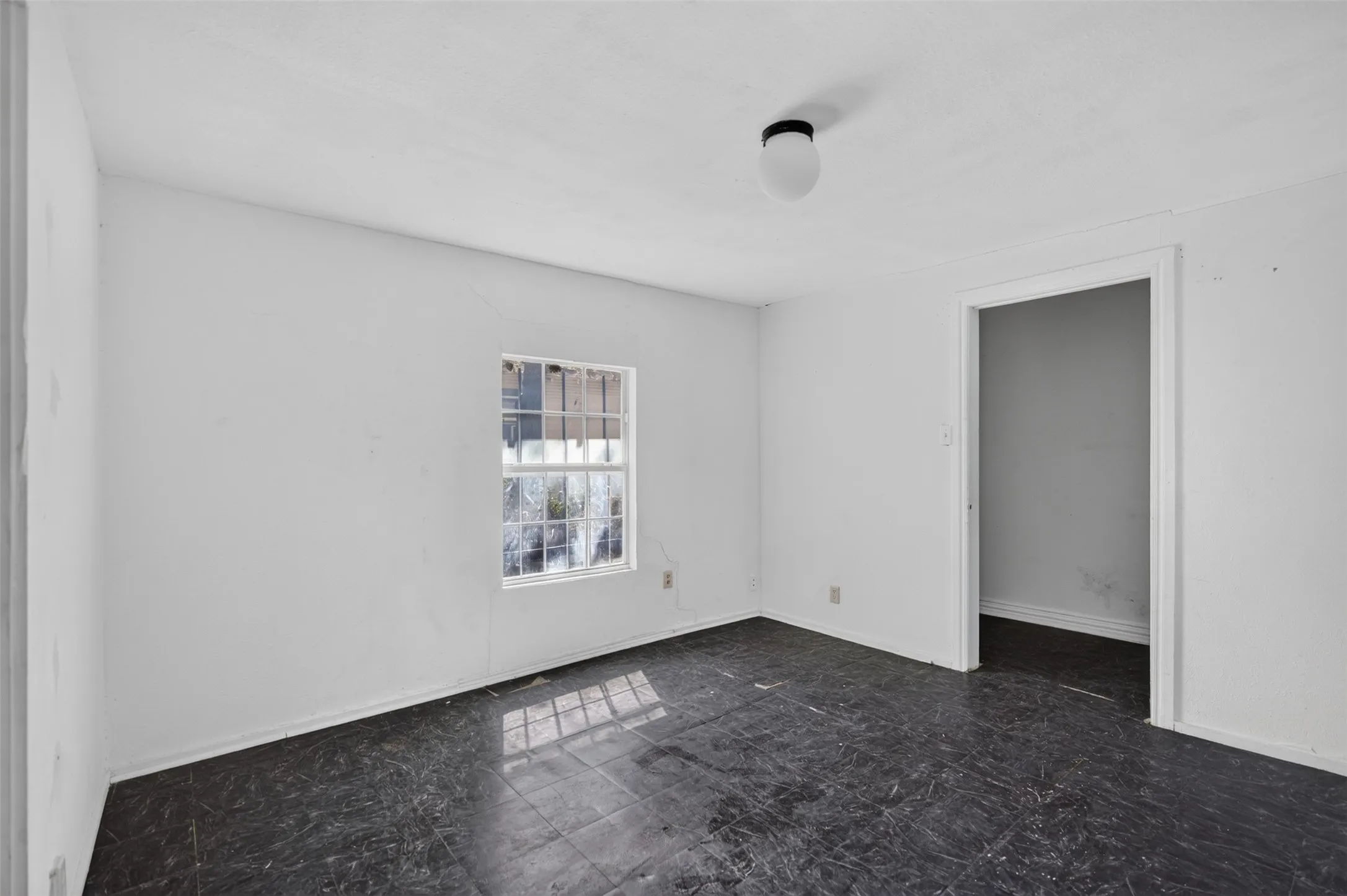 Room featuring a single window, white walls, dark-toned flooring, and a flush mount ceiling light