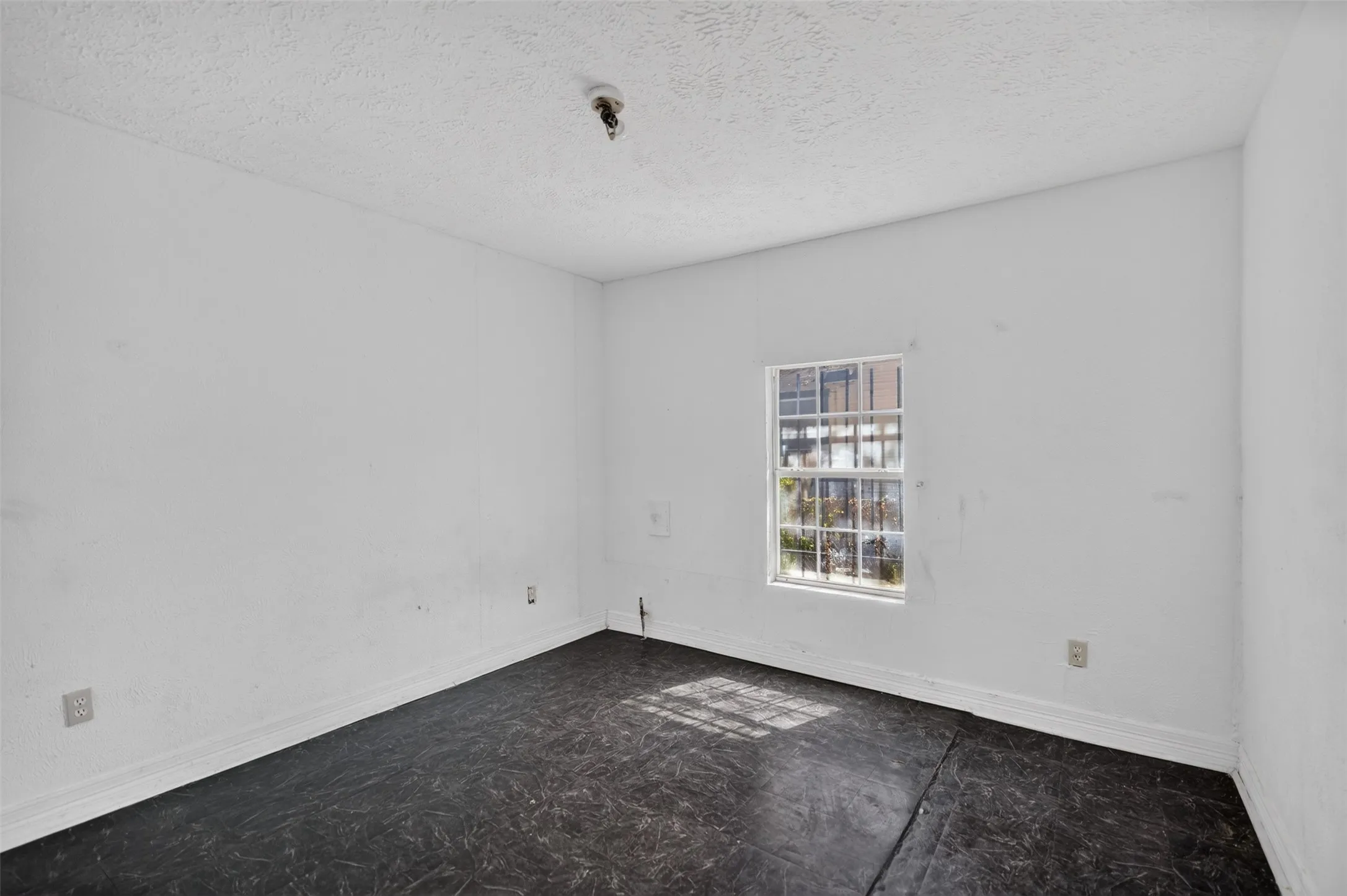 White painted walls with a single window and dark flooring