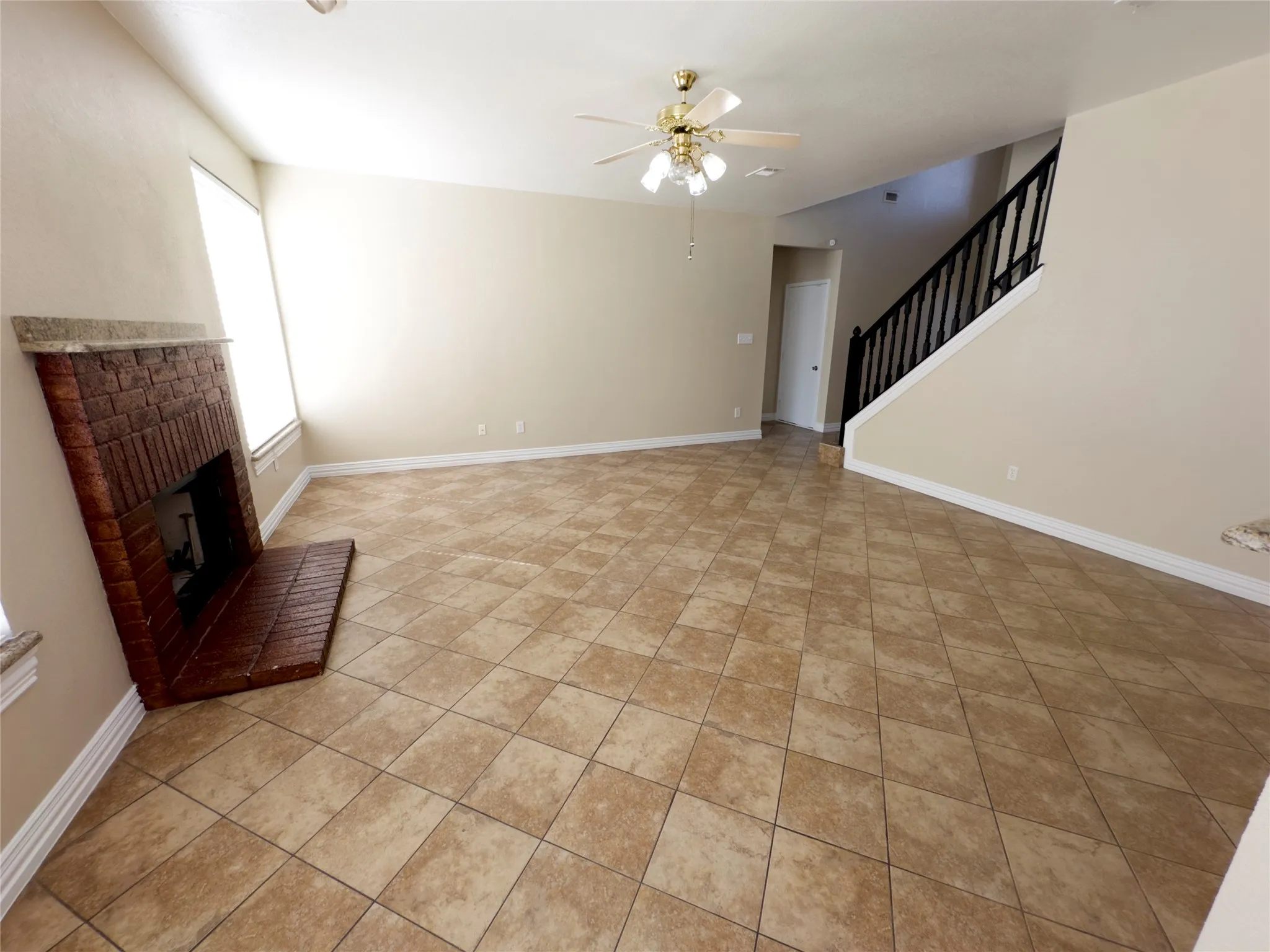 Unfurnished living room with stairway, a brick fireplace, a ceiling fan, and light tile patterned floors