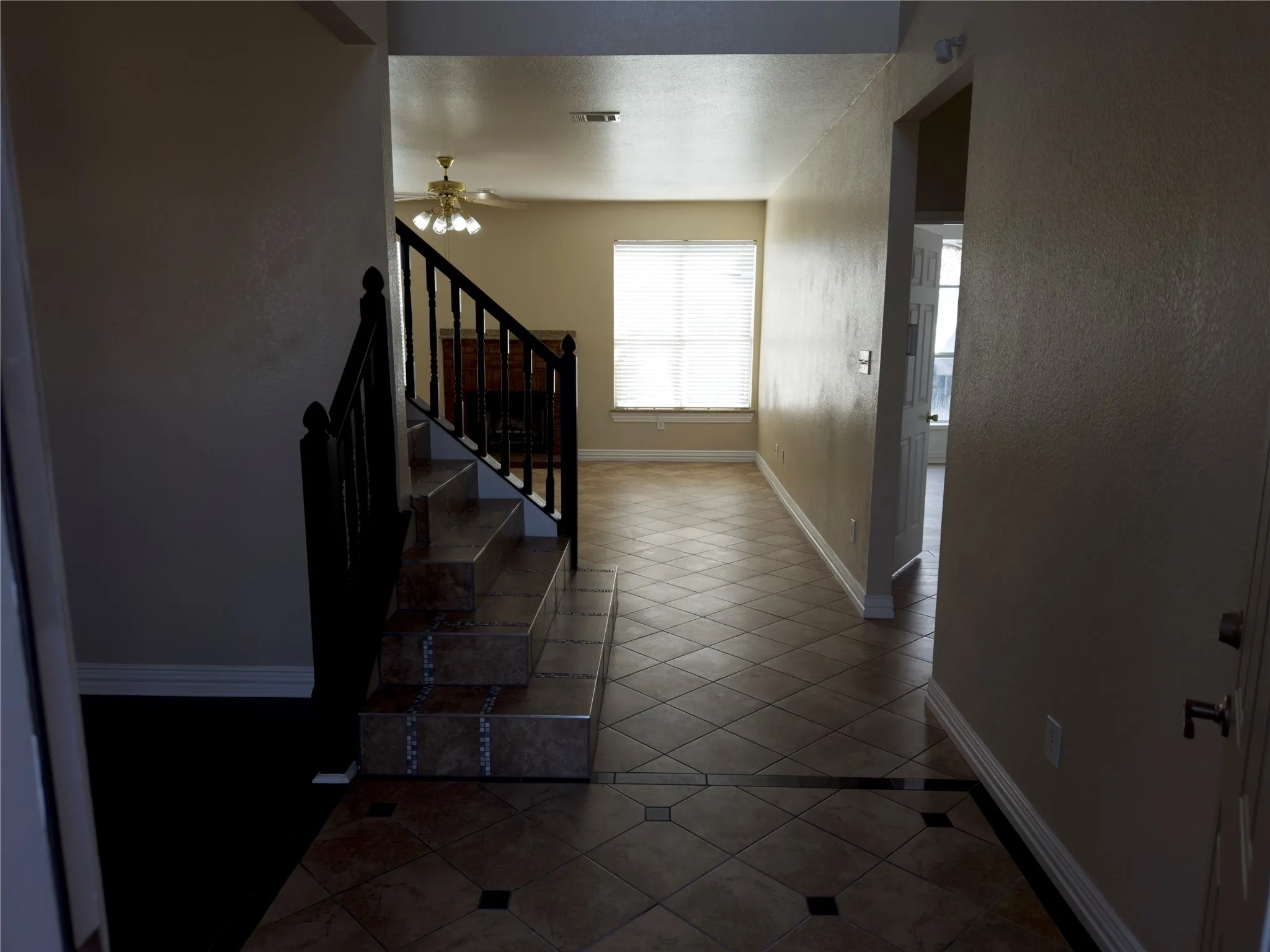 Foyer entrance with dark tile patterned floors, a textured wall, stairs, and ceiling fan