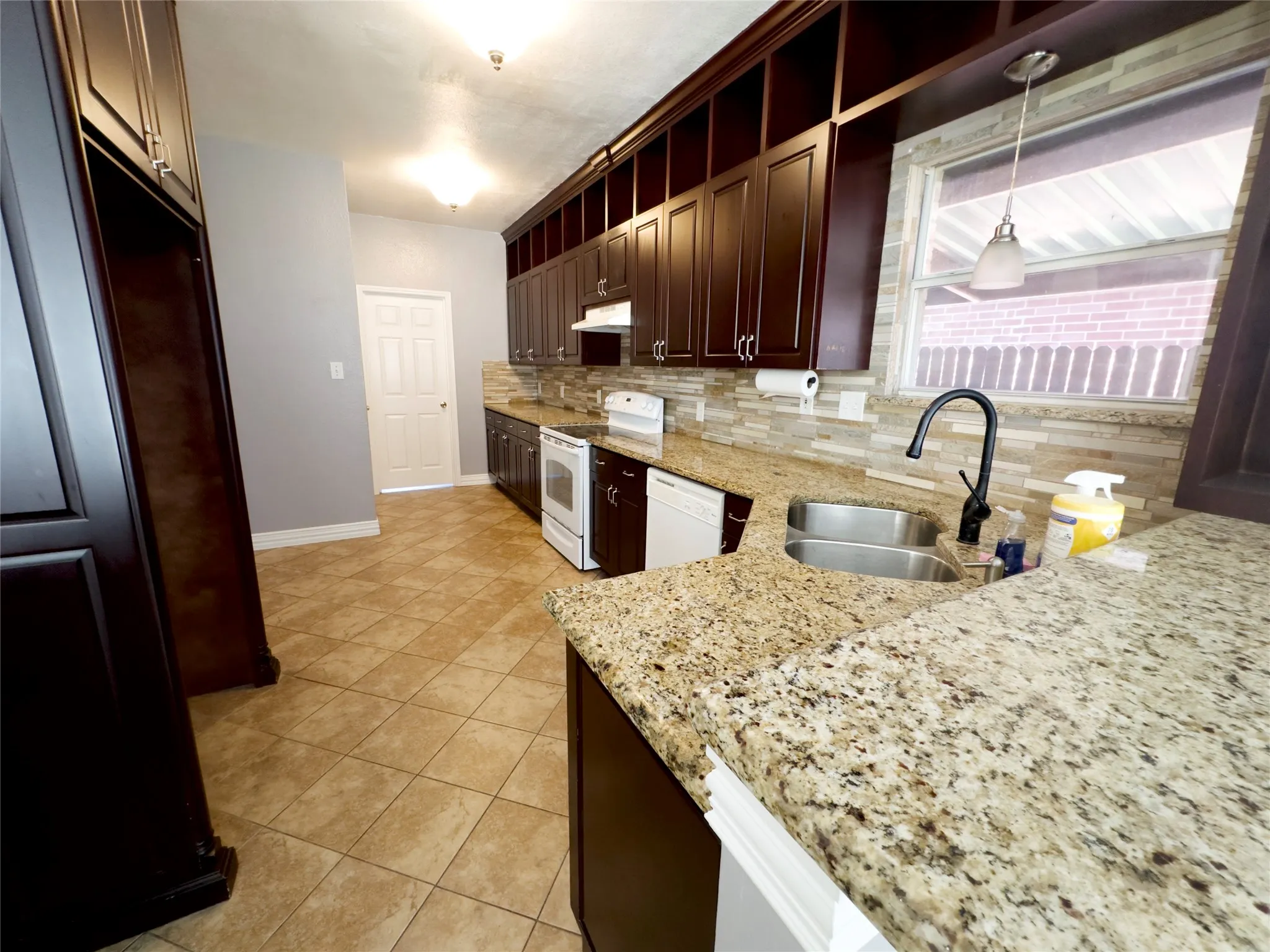 Kitchen with decorative backsplash, dark brown cabinets, white appliances, light stone counters, and light tile patterned floors