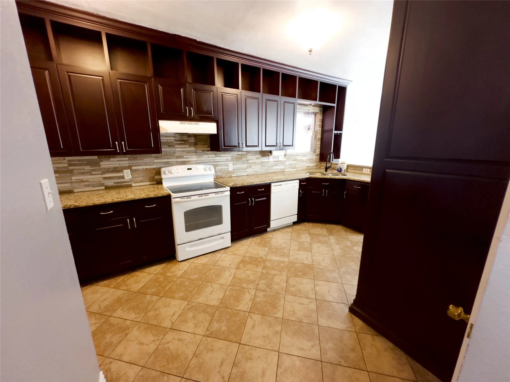 Kitchen featuring open shelves, dark brown cabinetry, white appliances, backsplash, and light stone countertops