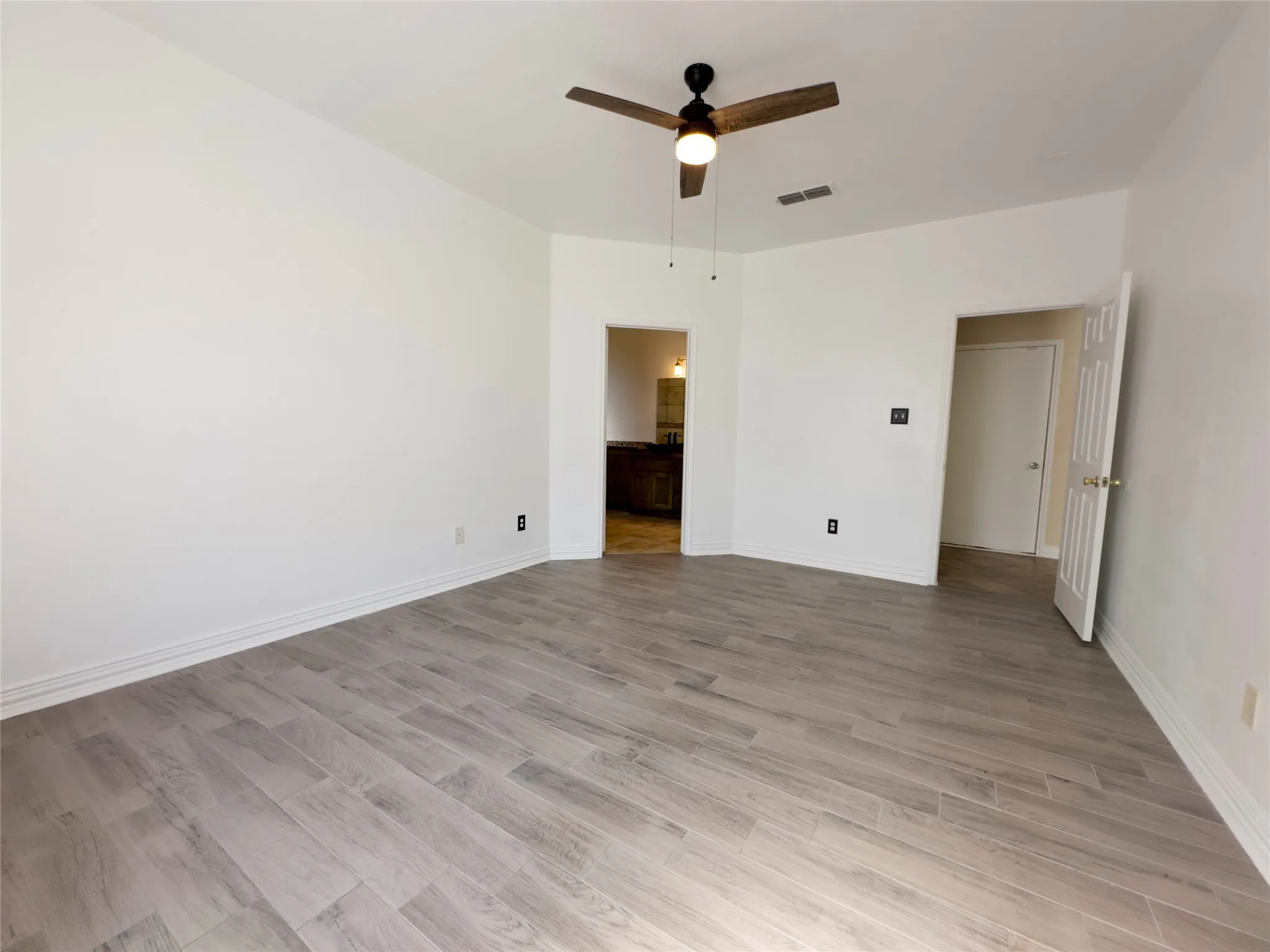 Unfurnished bedroom featuring light wood-style floors, a ceiling fan, and ensuite bath