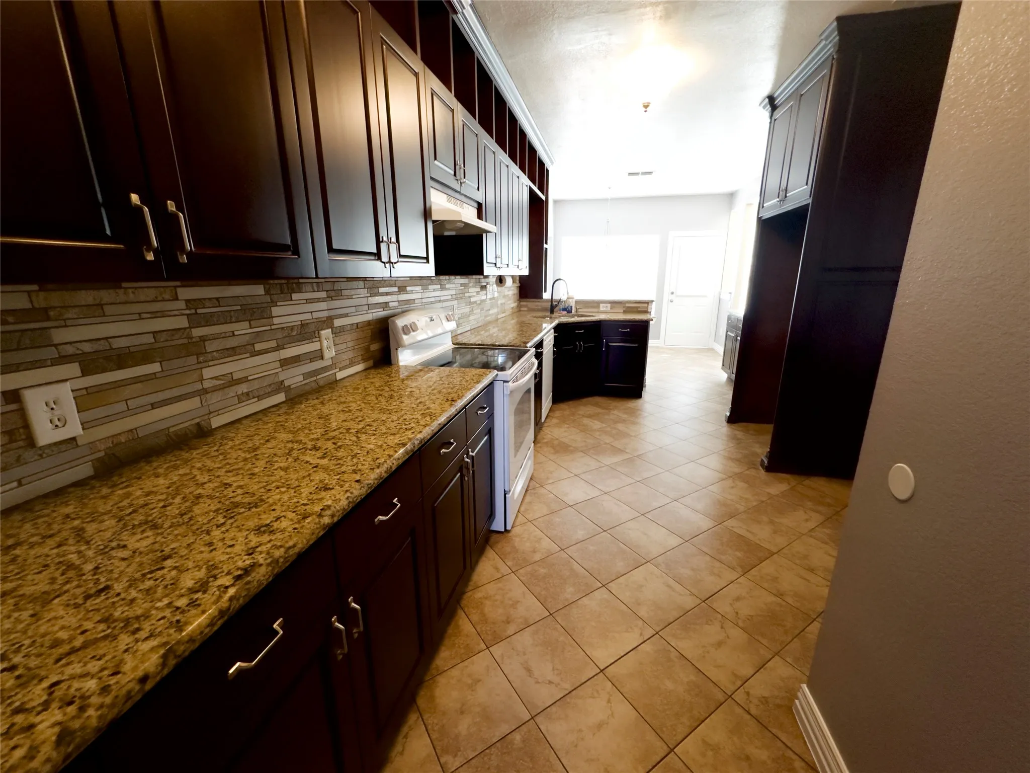 Kitchen featuring tasteful backsplash, white electric range, light tile patterned flooring, under cabinet range hood, and light stone countertops
