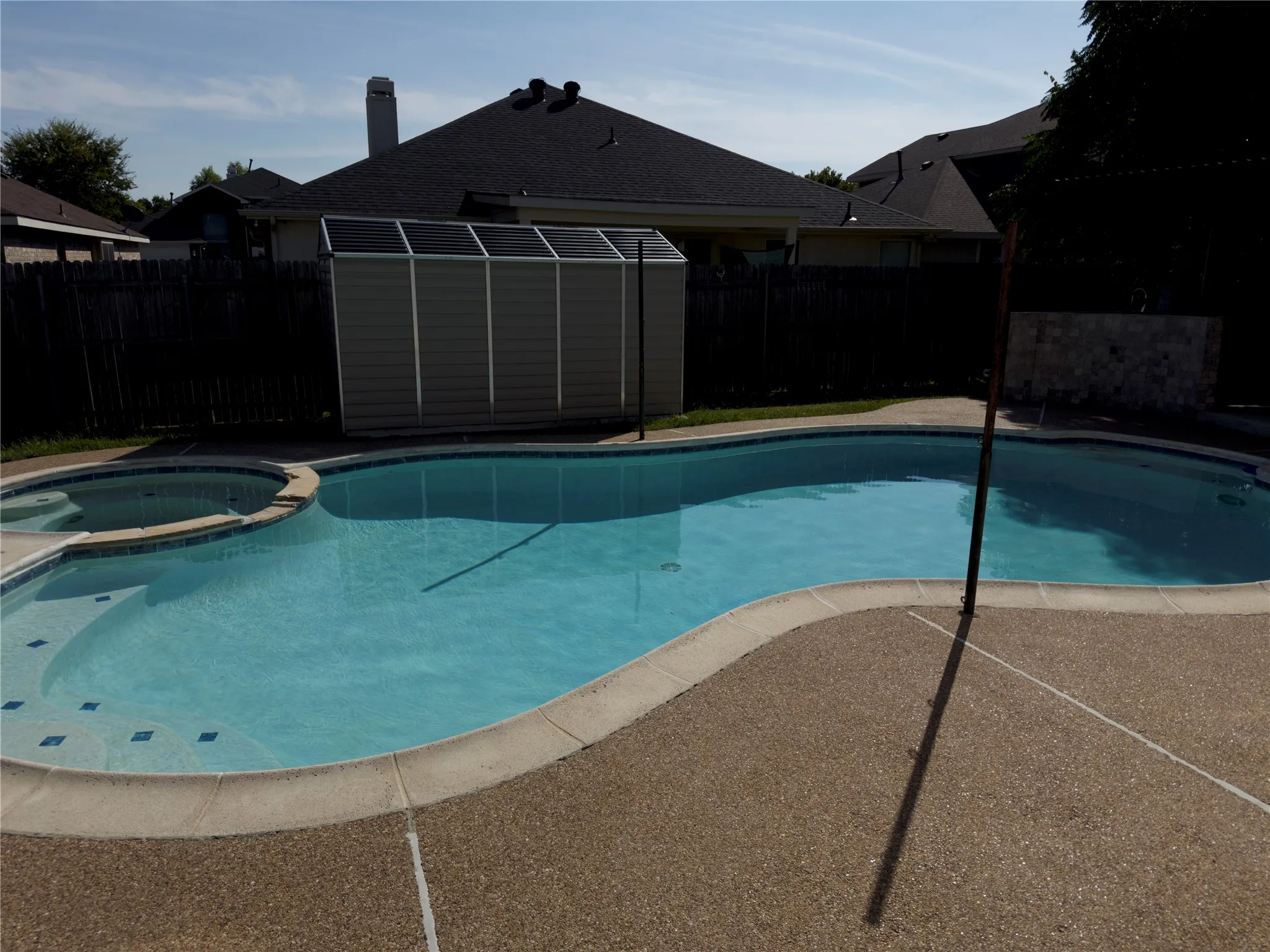 View of pool featuring a patio area, a pool with connected hot tub, a storage unit, and a fenced backyard
