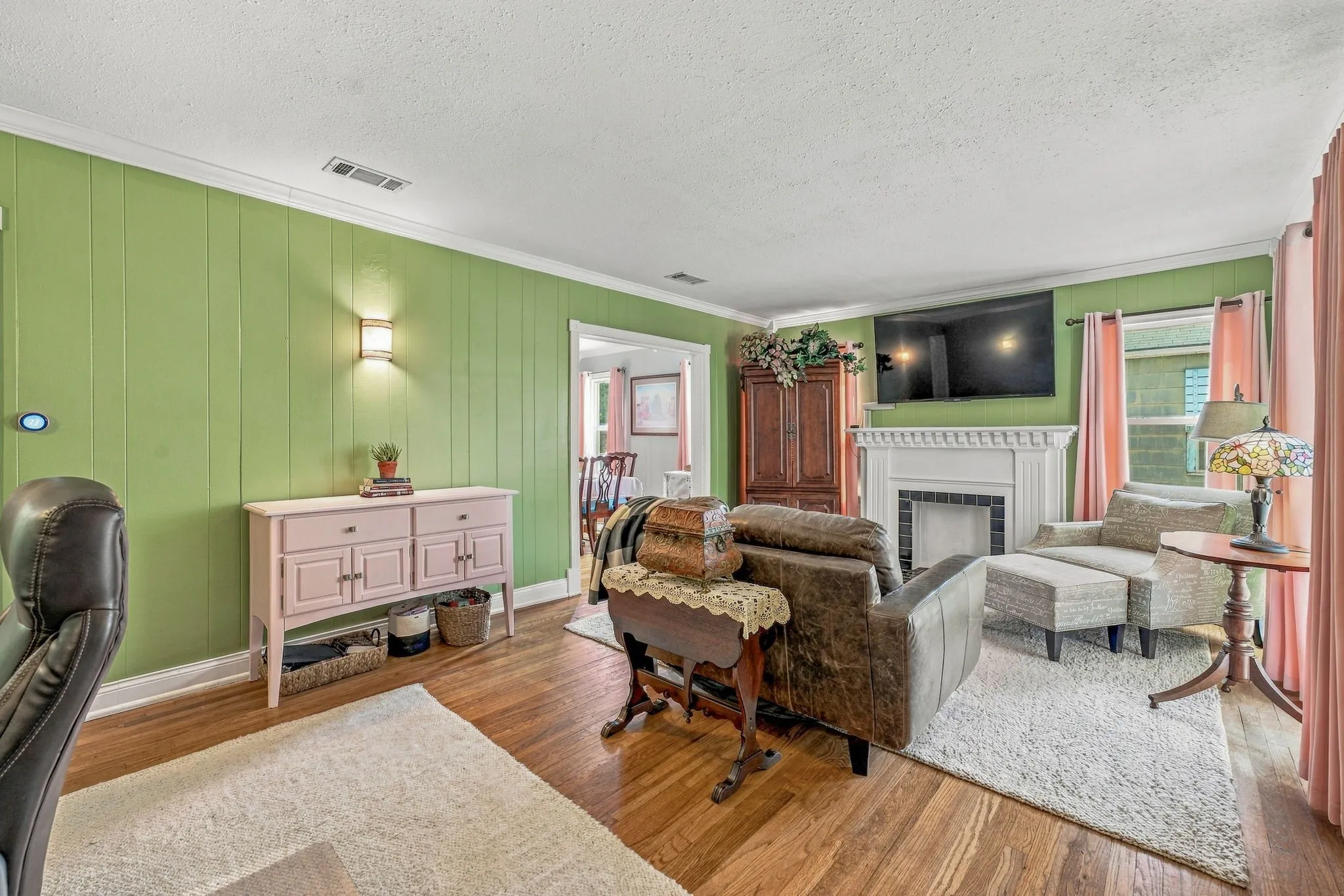 Large living room with original hardwood flooring, faux fireplace and multiple windows to let in abundant natural light.