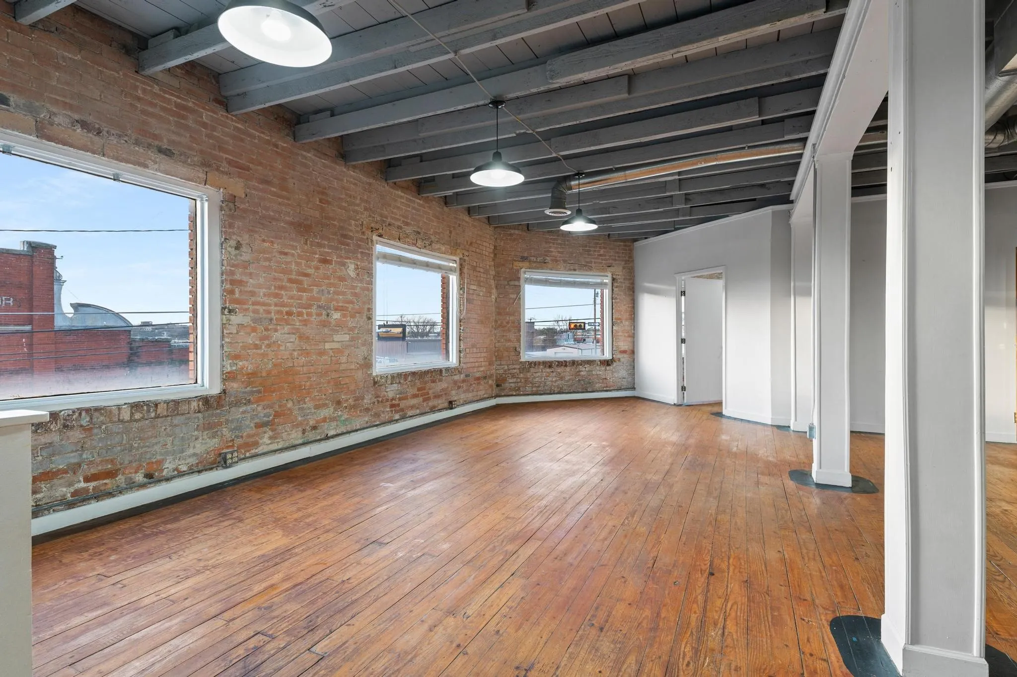 Exposed brick walls, wood-finish flooring, multiple windows, industrial pendant lighting, and exposed ceiling joists