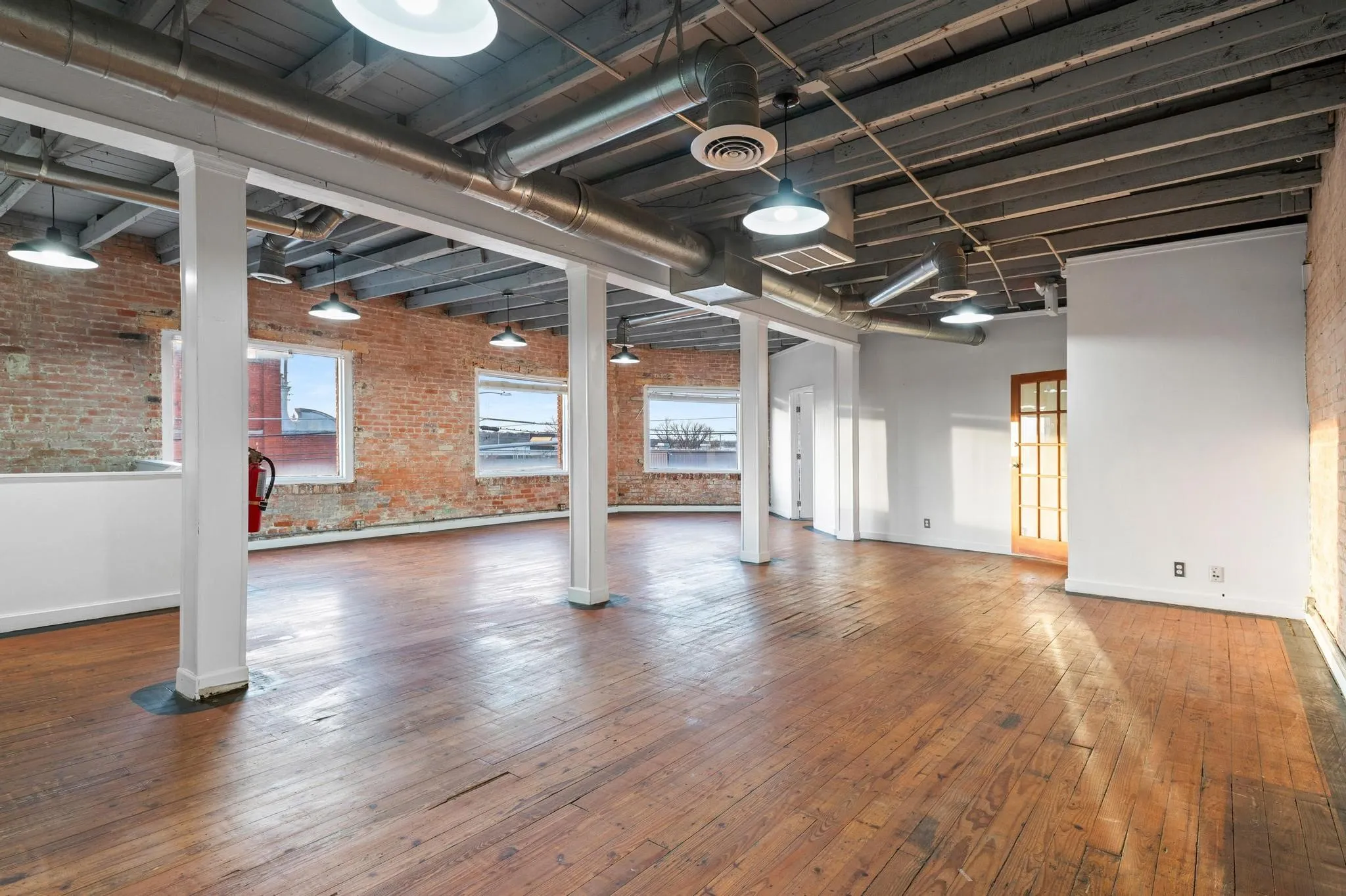 Exposed brick walls, wood-finish flooring, industrial ceiling with exposed ductwork, multiple windows, and a wood-frame door