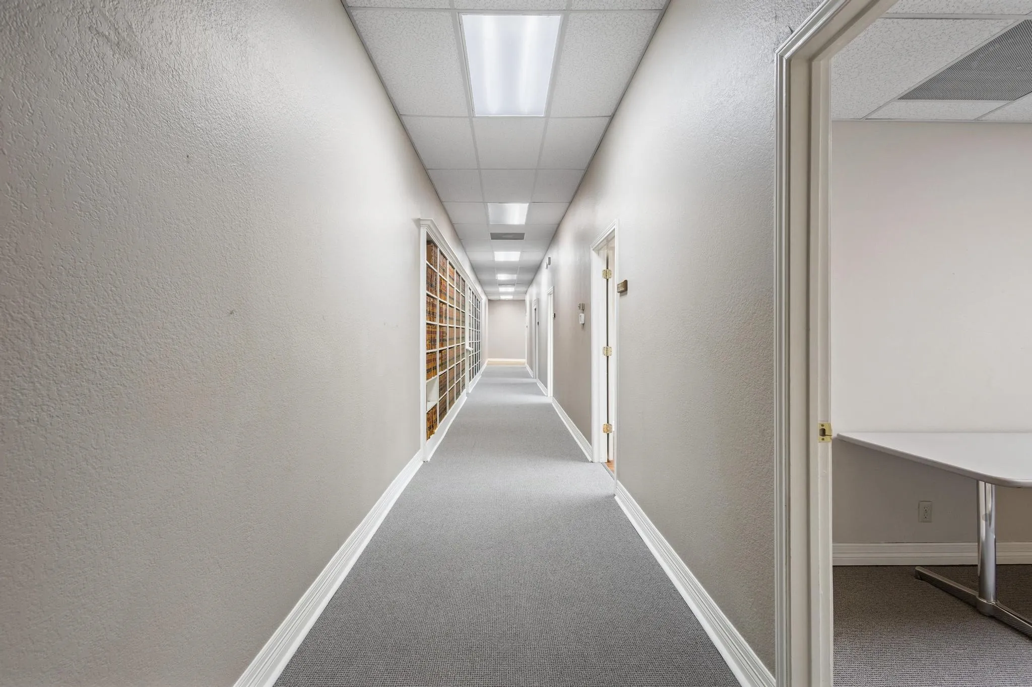 Long hallway with neutral wall paint, carpet flooring, a drop ceiling, and recessed lighting