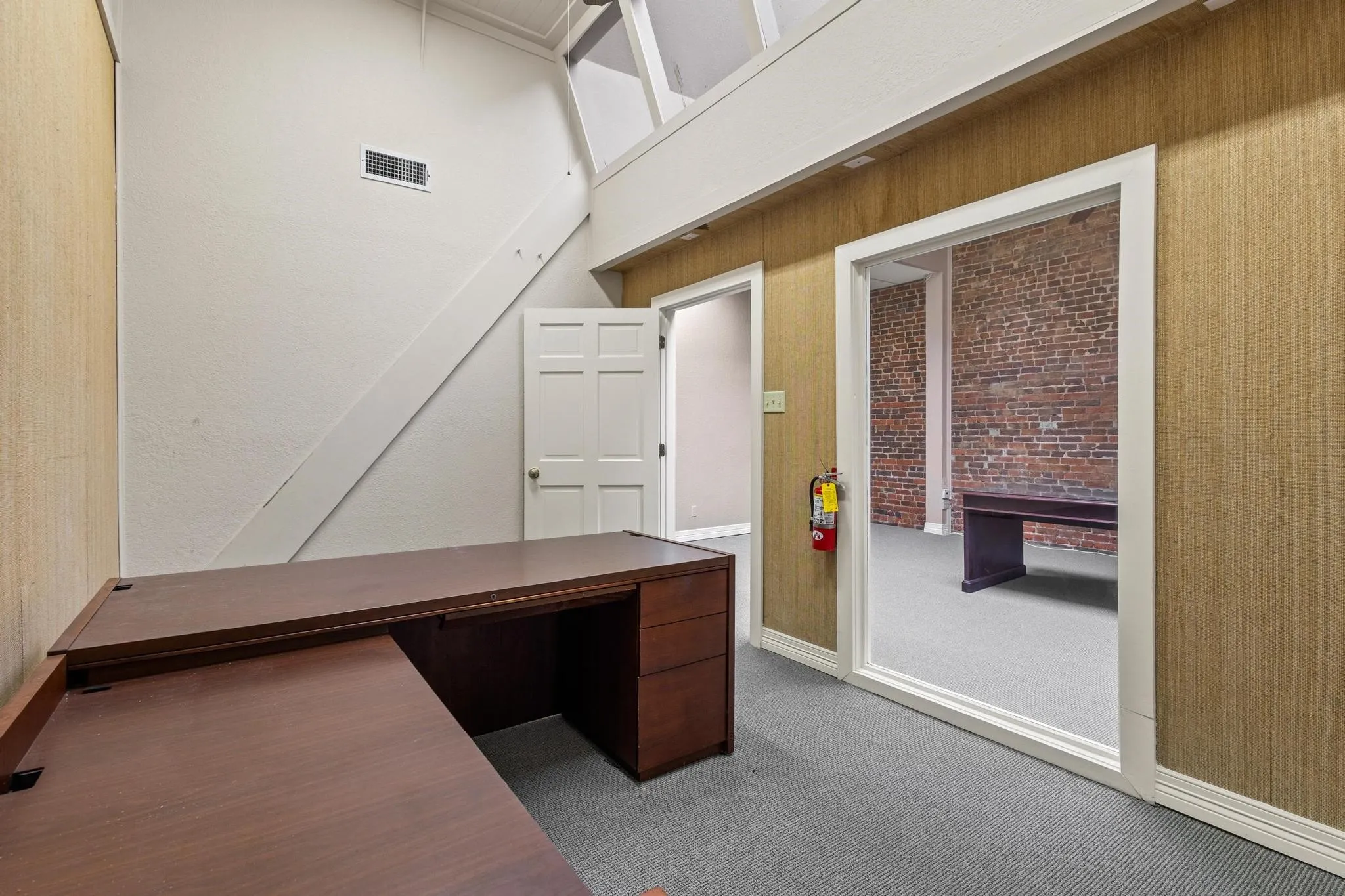 Vaulted ceiling with exposed beam, textured wall covering, and interior window
