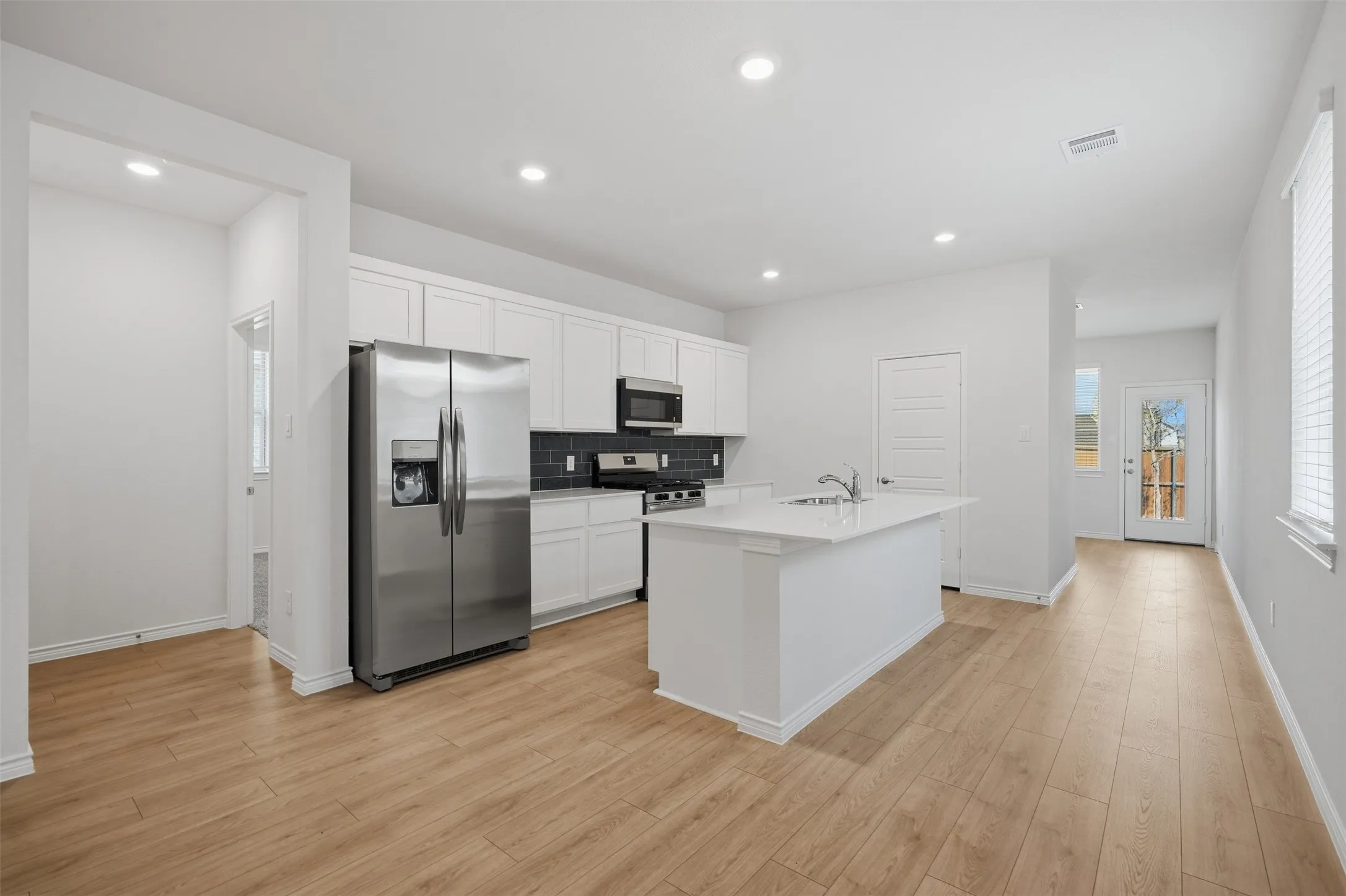 Open-concept kitchen featuring wood-finish flooring, white cabinetry, stainless steel appliances, a center island with sink, and recessed lighting