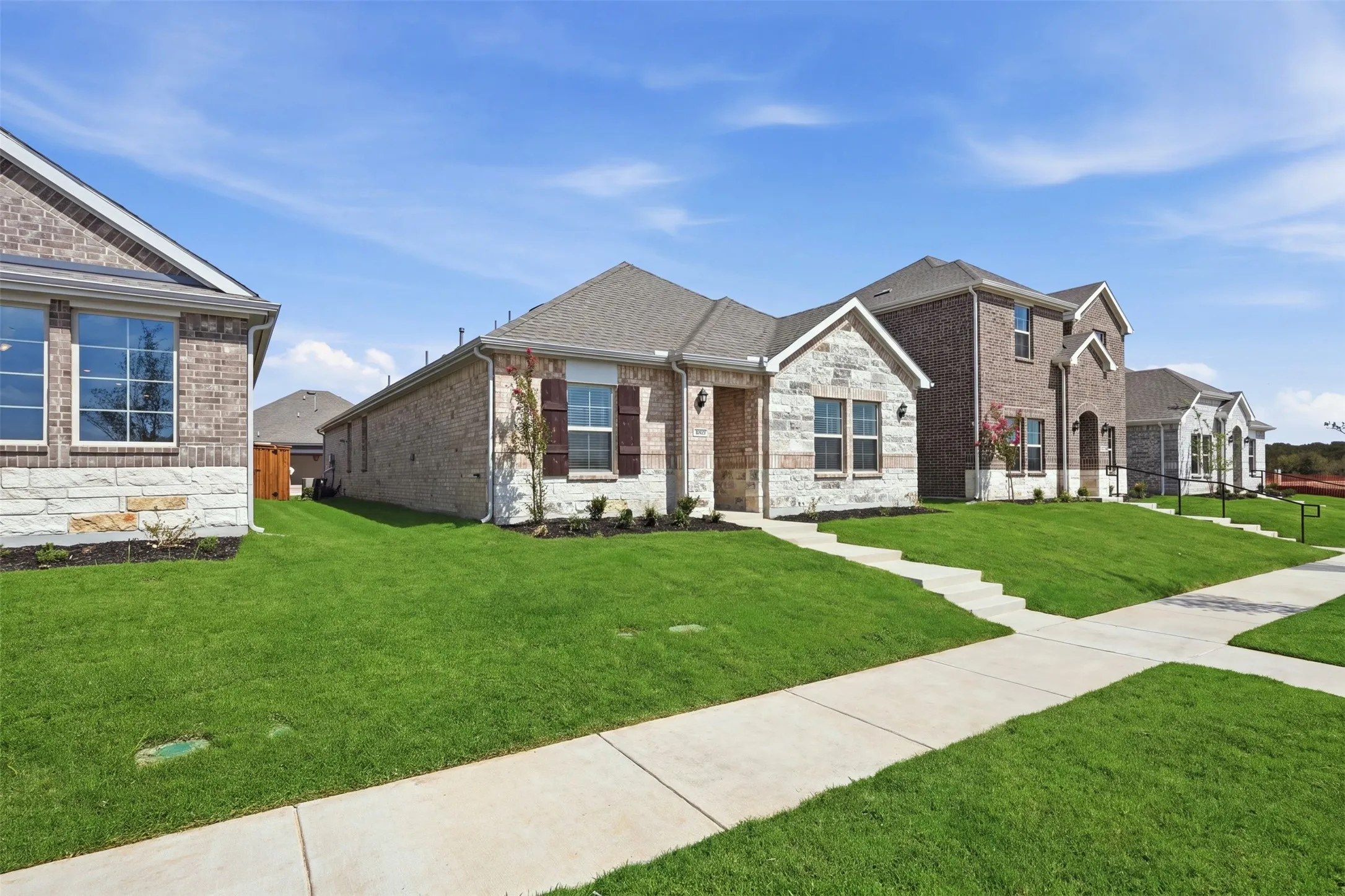 Stone and brick facade with dark shutters, gabled roofline, and front landscaping