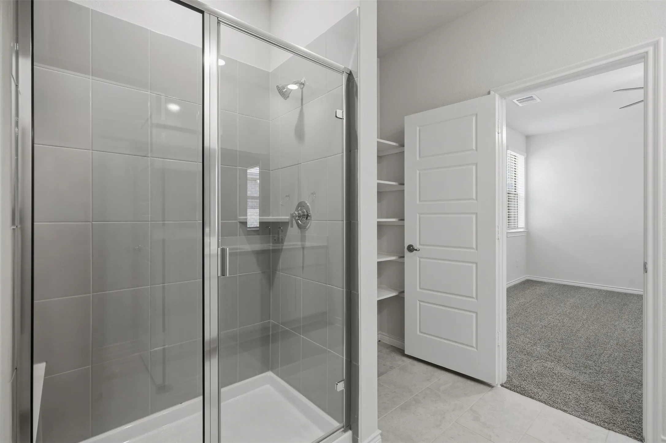 Glass-enclosed shower with gray tiled walls and a built-in bench