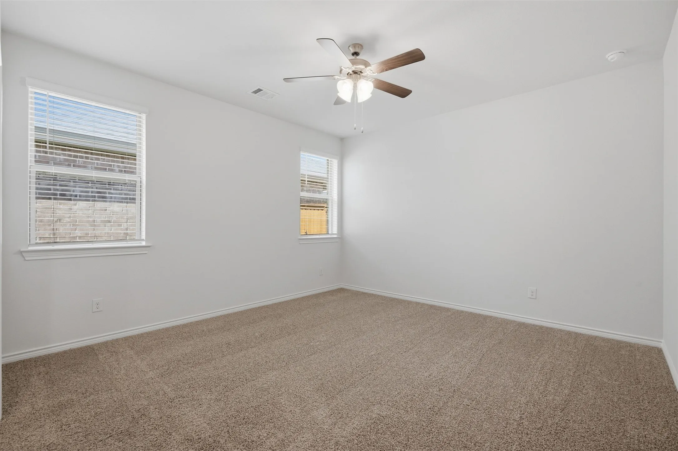 Neutral wall paint, two windows with blinds, ceiling fan with integrated lighting, and carpet flooring