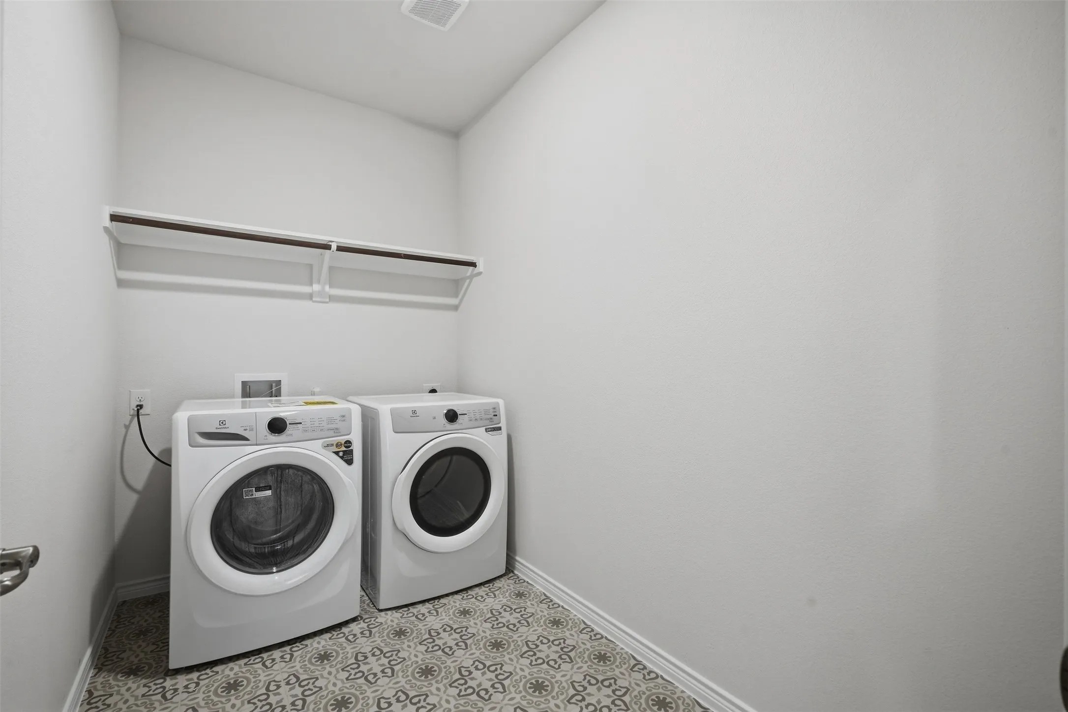 Laundry area featuring patterned floor tile, white walls, and a built-in shelf with hanging rod
