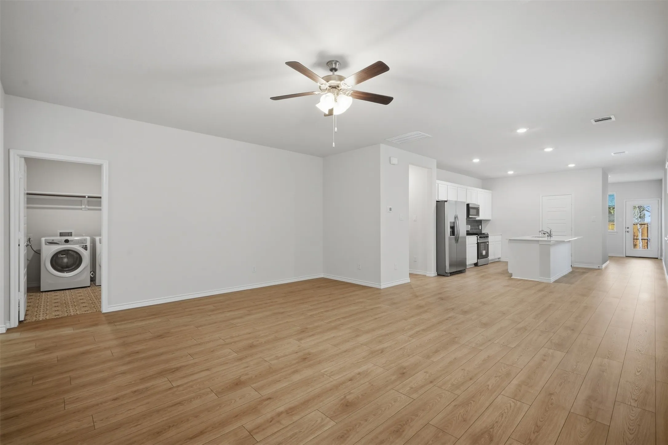 Wood-finish flooring throughout, ceiling fan with integrated lighting, recessed lighting, white cabinetry, and stainless steel kitchen appliances