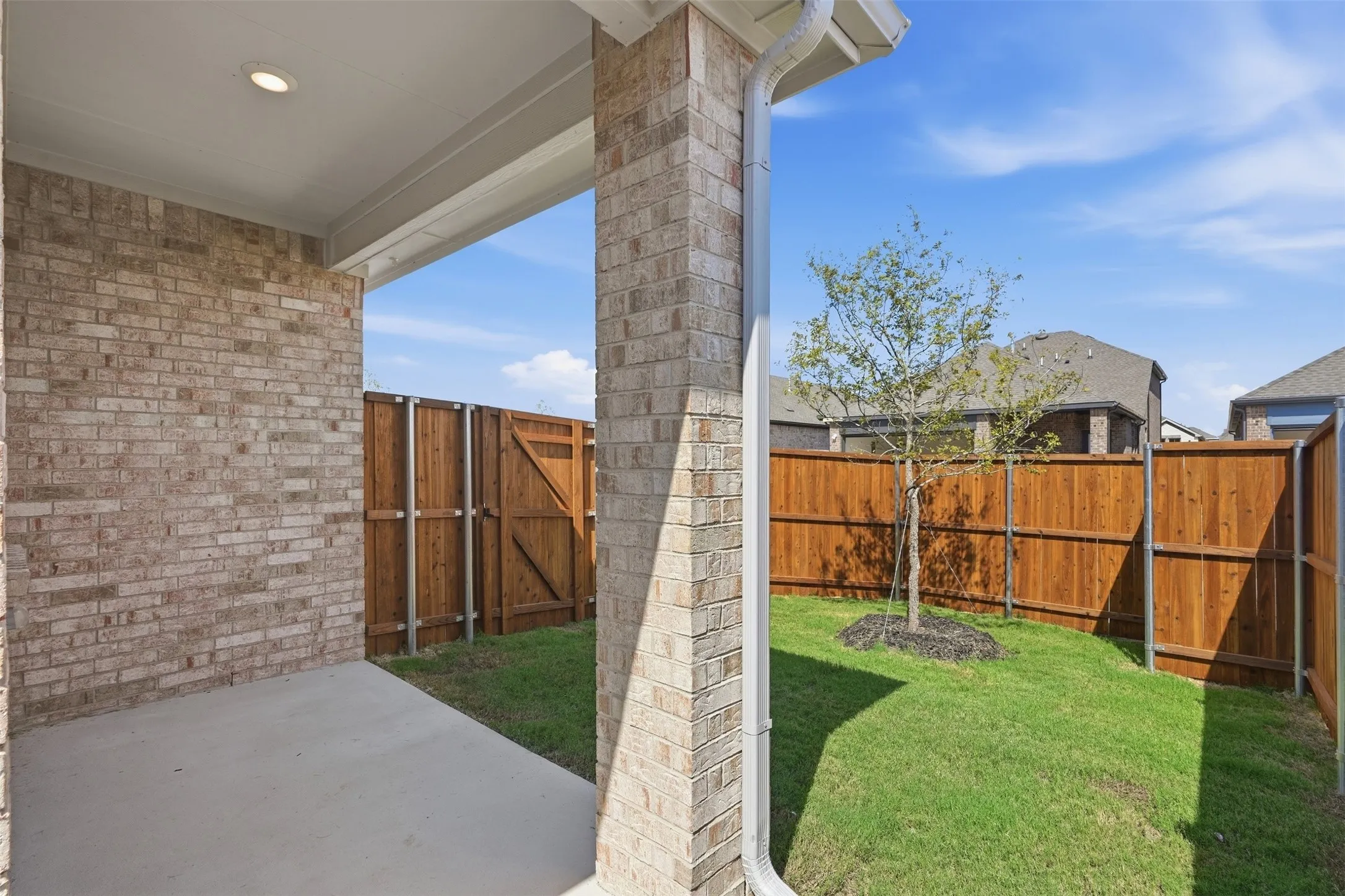 Covered patio with a concrete surface, featuring brick columns and a recessed light