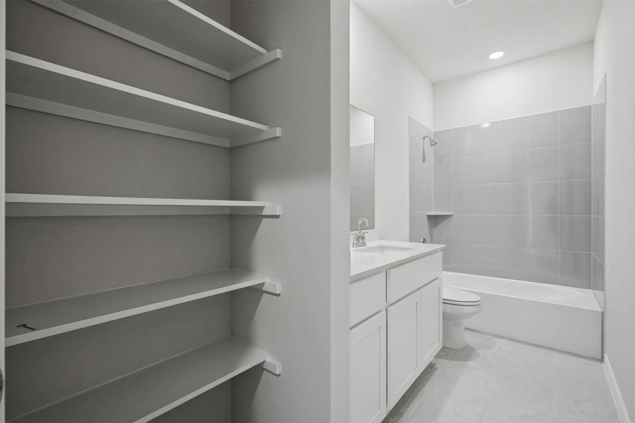 Full bathroom featuring a white vanity with an integrated sink, a built-in tub with tile surround, and a separate storage closet with multiple shelves