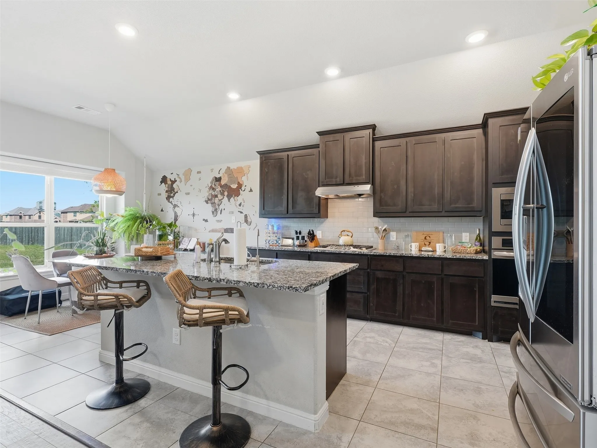Kitchen featuring dark wood-finish cabinetry, stainless steel appliances, a tile backsplash, and a large center island with a granite countertop