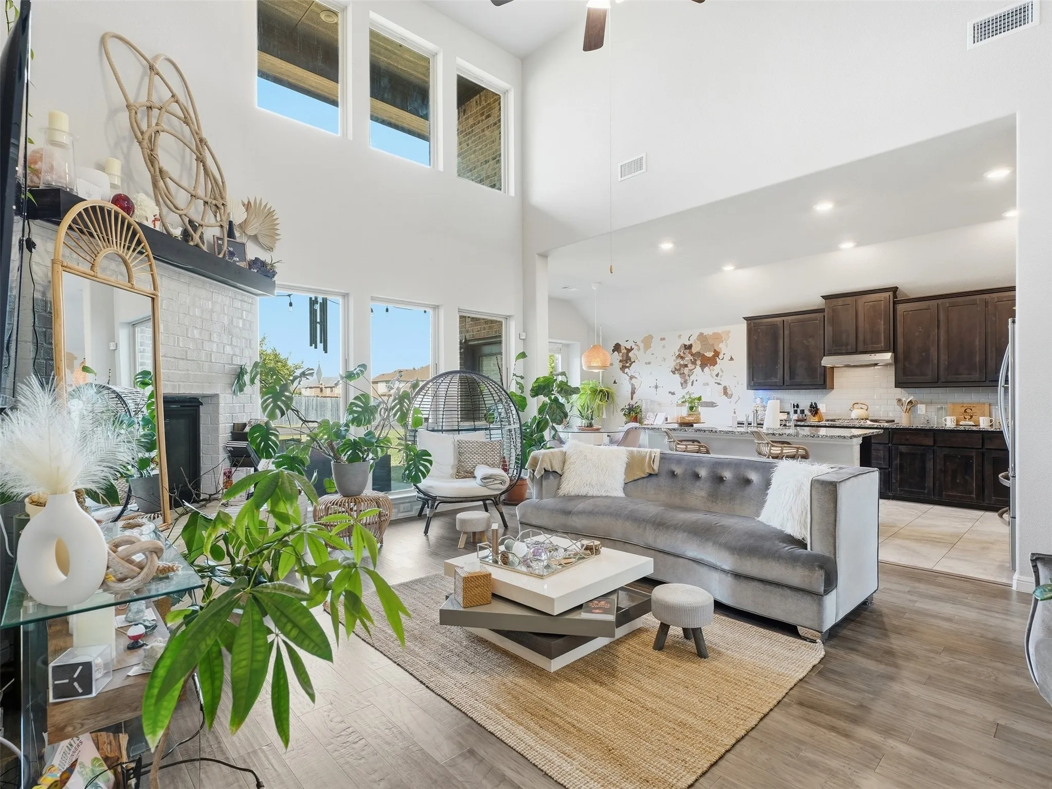 Two-story living area with high ceilings, an integrated kitchen, a fireplace with a white brick surround, and large windows