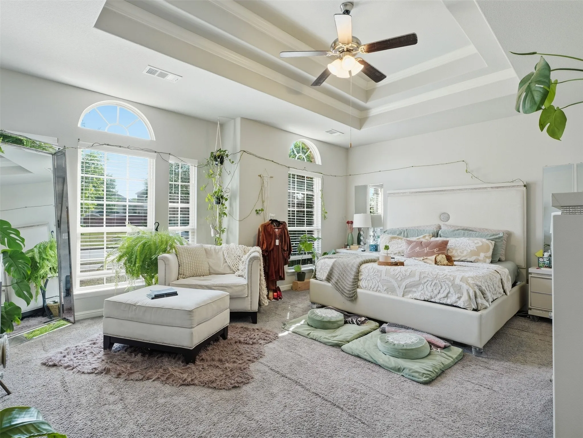 Tray ceiling with a ceiling fan, arched transom windows, and wall-to-wall carpeting