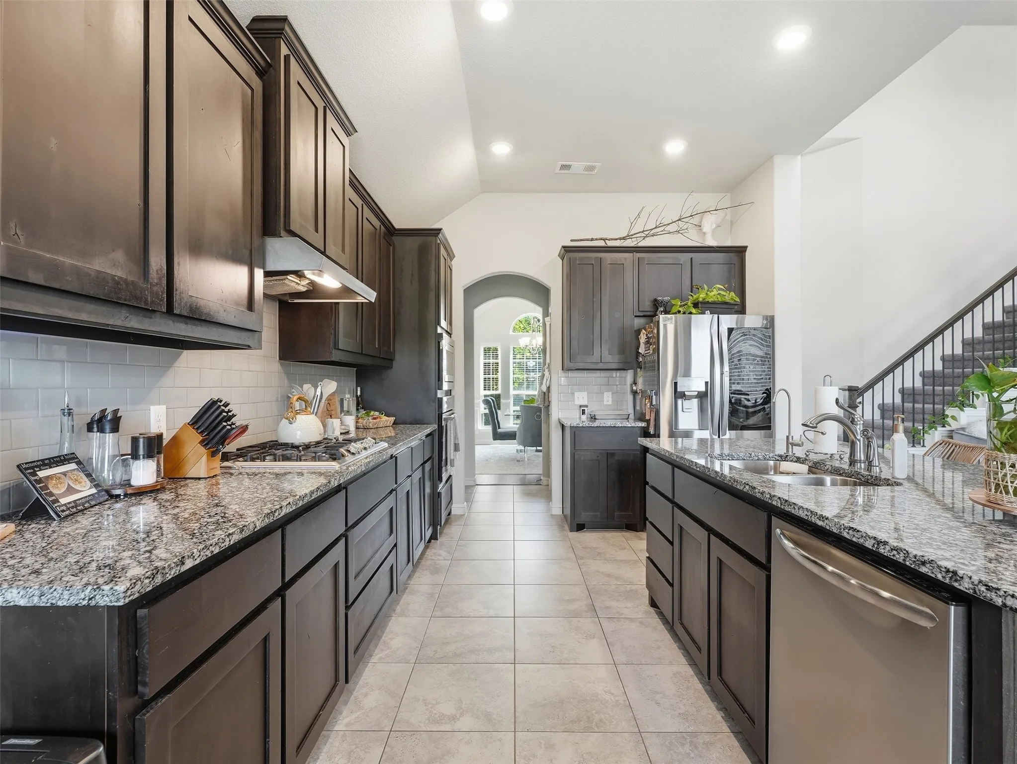 Galley kitchen with dark wood-finish cabinetry, light-toned granite countertops, and stainless steel appliances