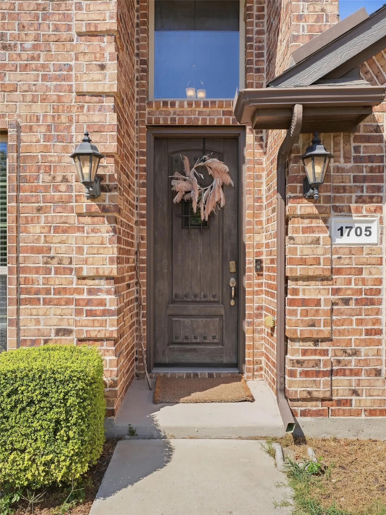Brick exterior facade with a paneled wood entry door, transom window, and architectural overhang