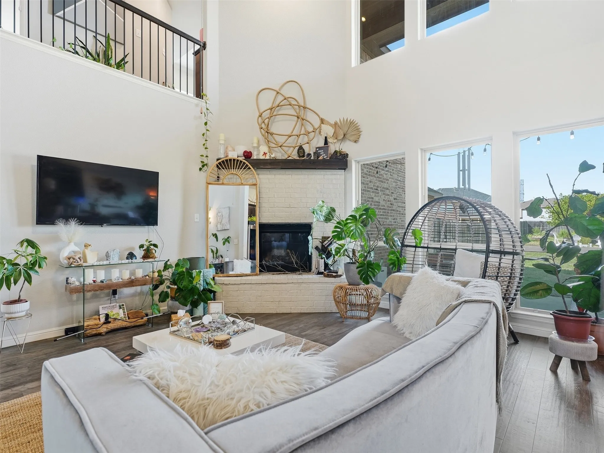 Two-story living area with high ceilings, featuring a fireplace with a white brick surround, large windows, and wood-finish flooring