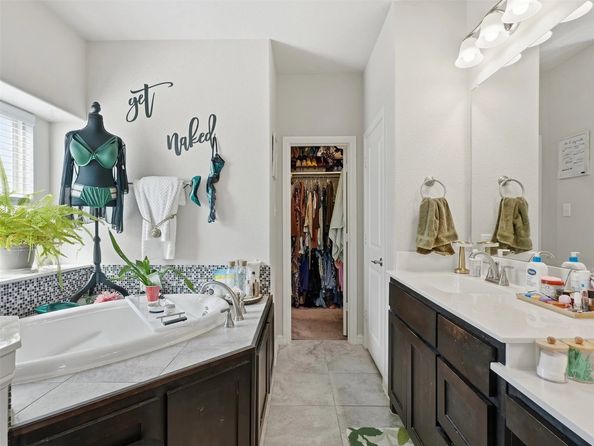 Enclosed walk-in closet, dual vanity with solid surface countertop, soaker tub with tile surround, mosaic tile backsplash, and tile flooring