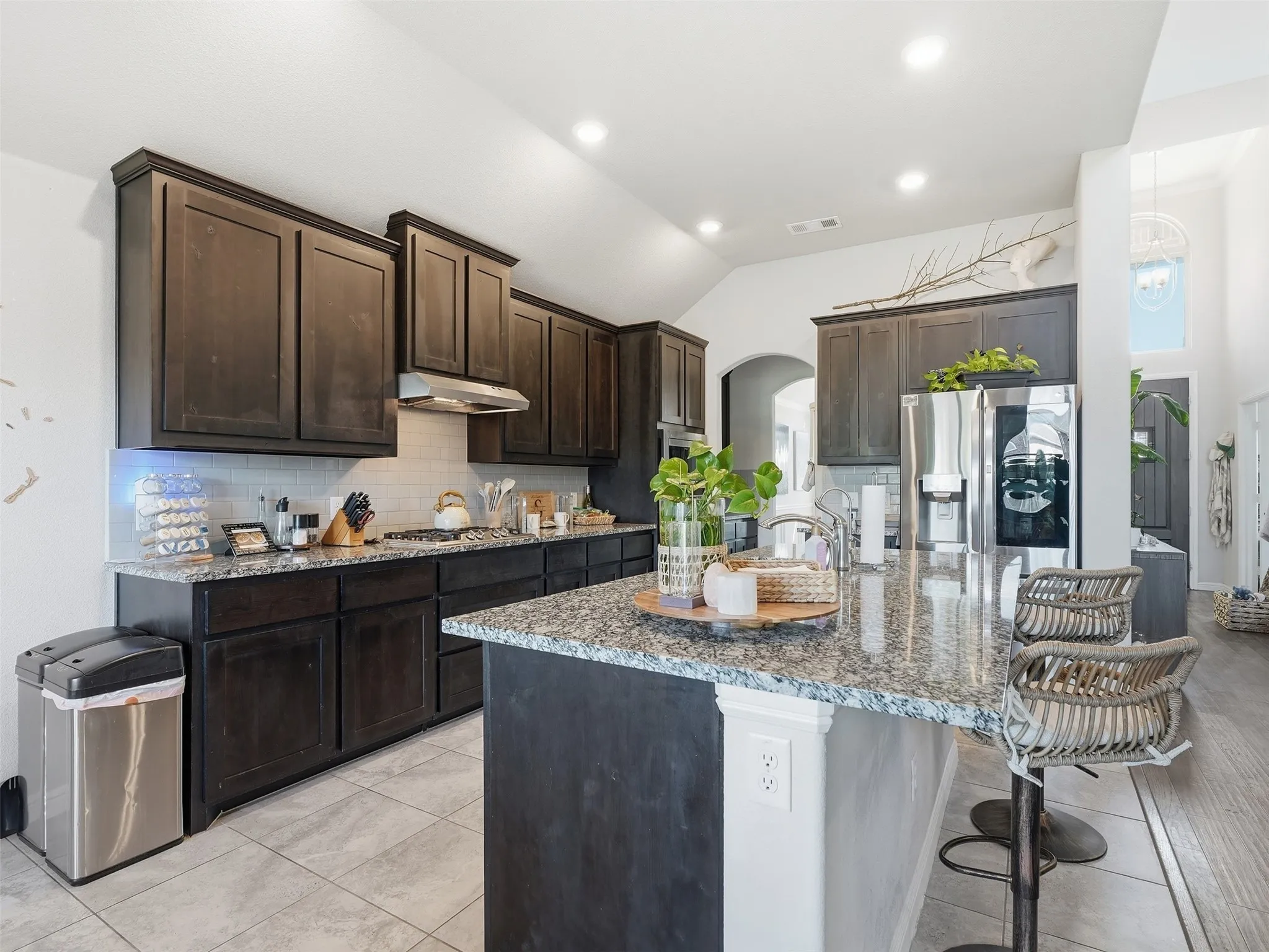 Kitchen featuring dark wood cabinetry, light granite countertops, stainless steel appliances, a tiled backsplash, and recessed lighting