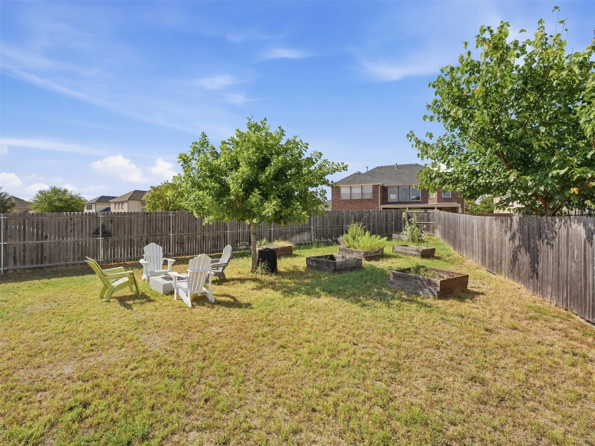 Expansive fenced backyard featuring mature trees, raised garden beds, and a designated seating area
