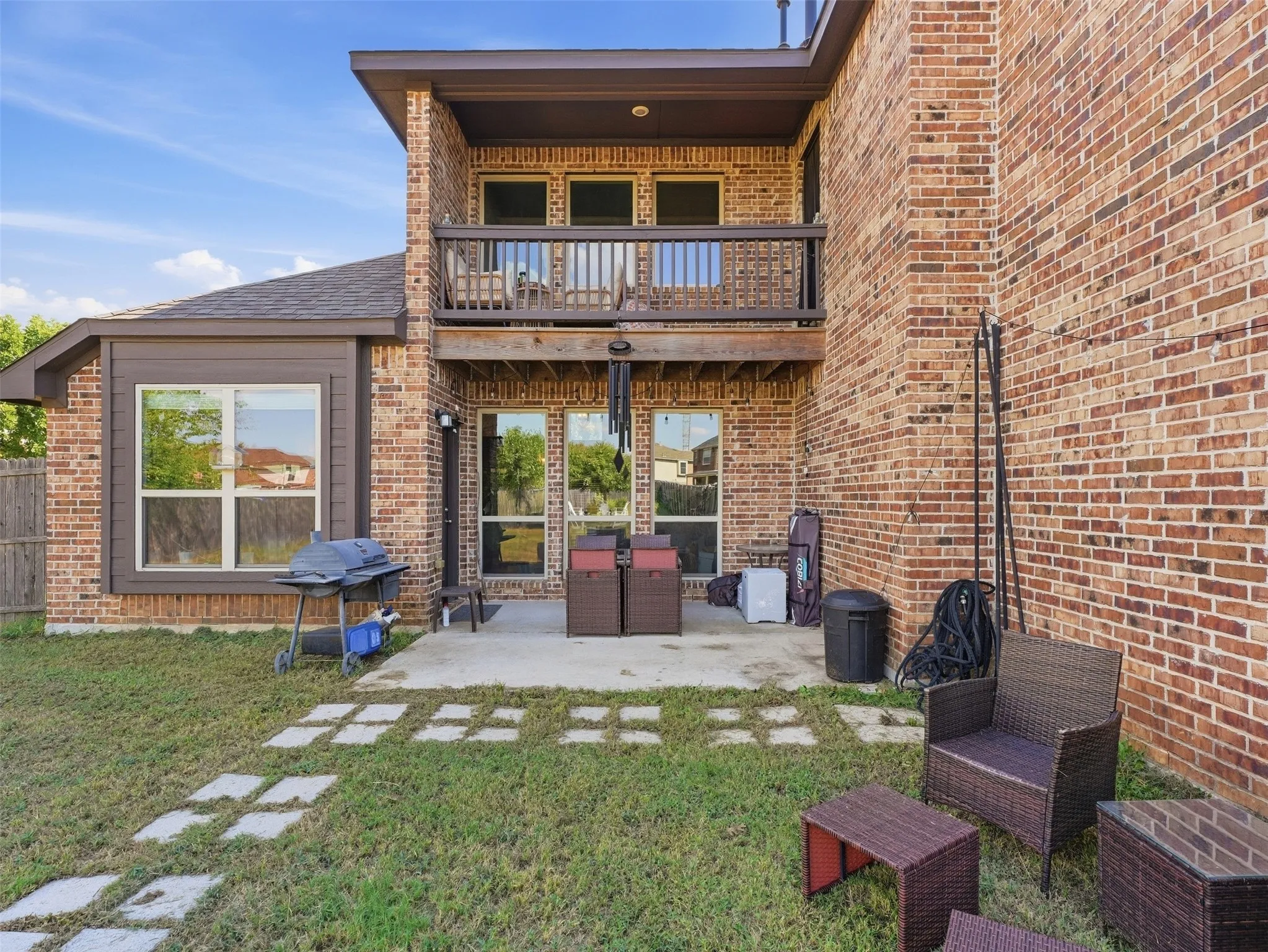 Brick exterior with an upper-level balcony, ground-level patio, and square stepping stones