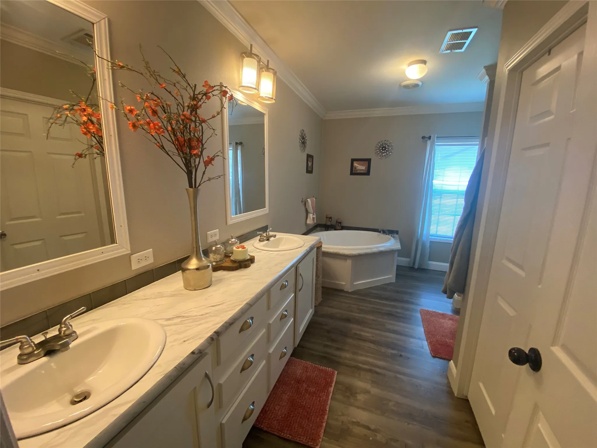 Bathroom with double vanity, ornamental molding, a soaking tub, and dark wood-type flooring