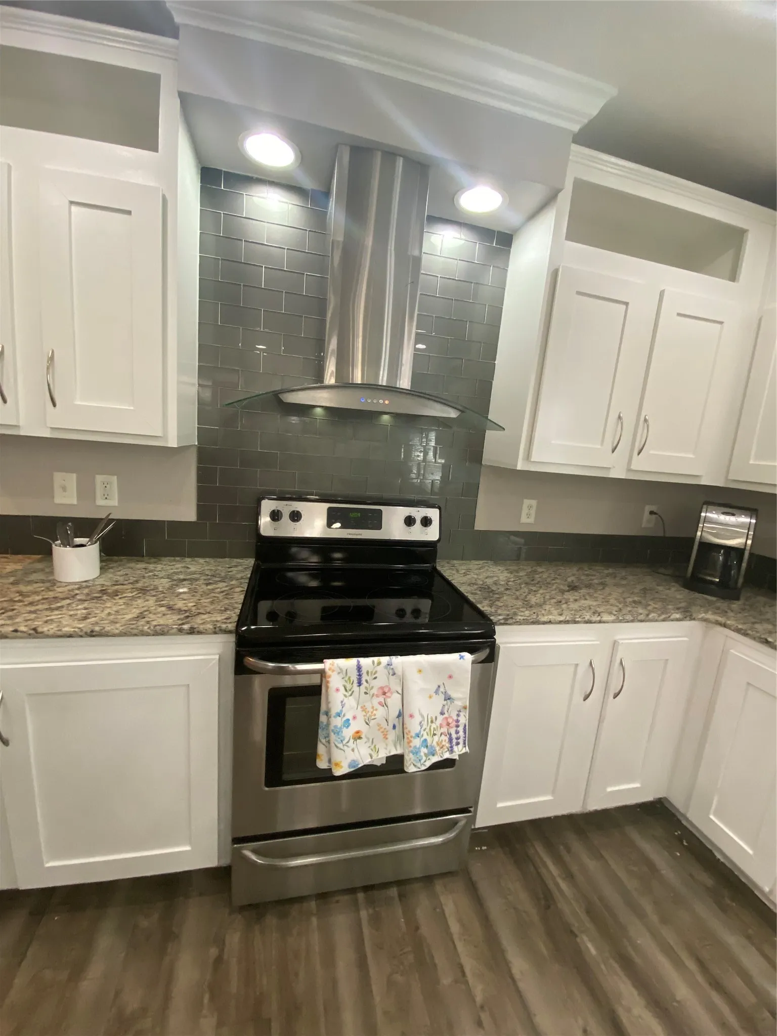 Kitchen with electric stove, white cabinets, extractor fan, dark stone counters, and glass insert cabinets