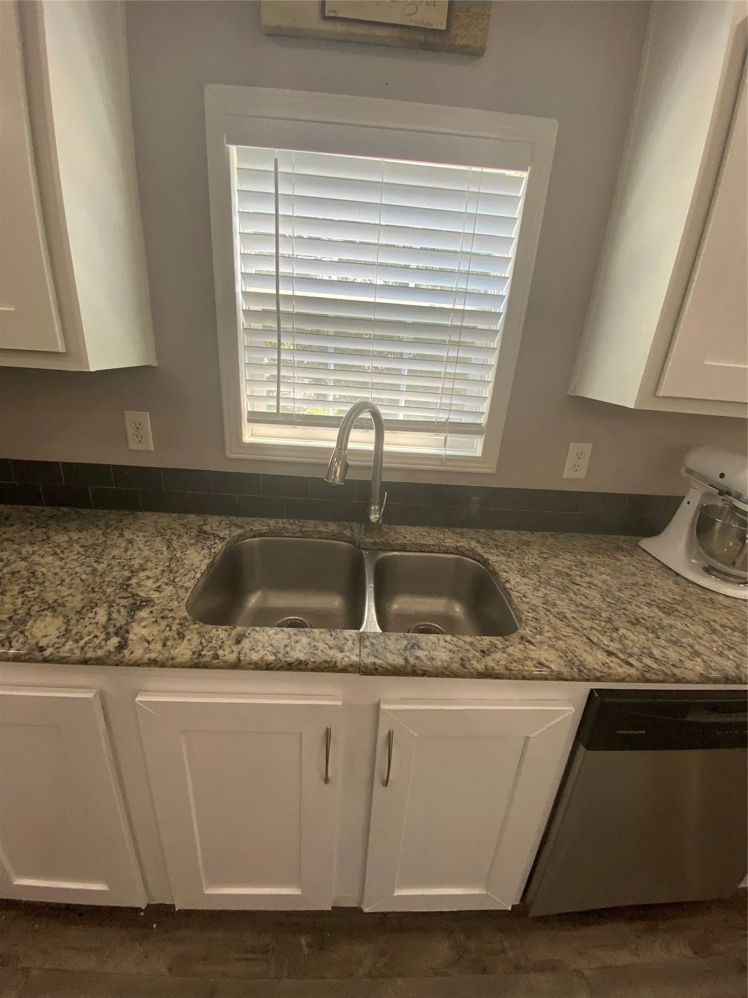 Kitchen with white cabinetry, dishwashing machine, dark stone countertops, and dark wood-type flooring