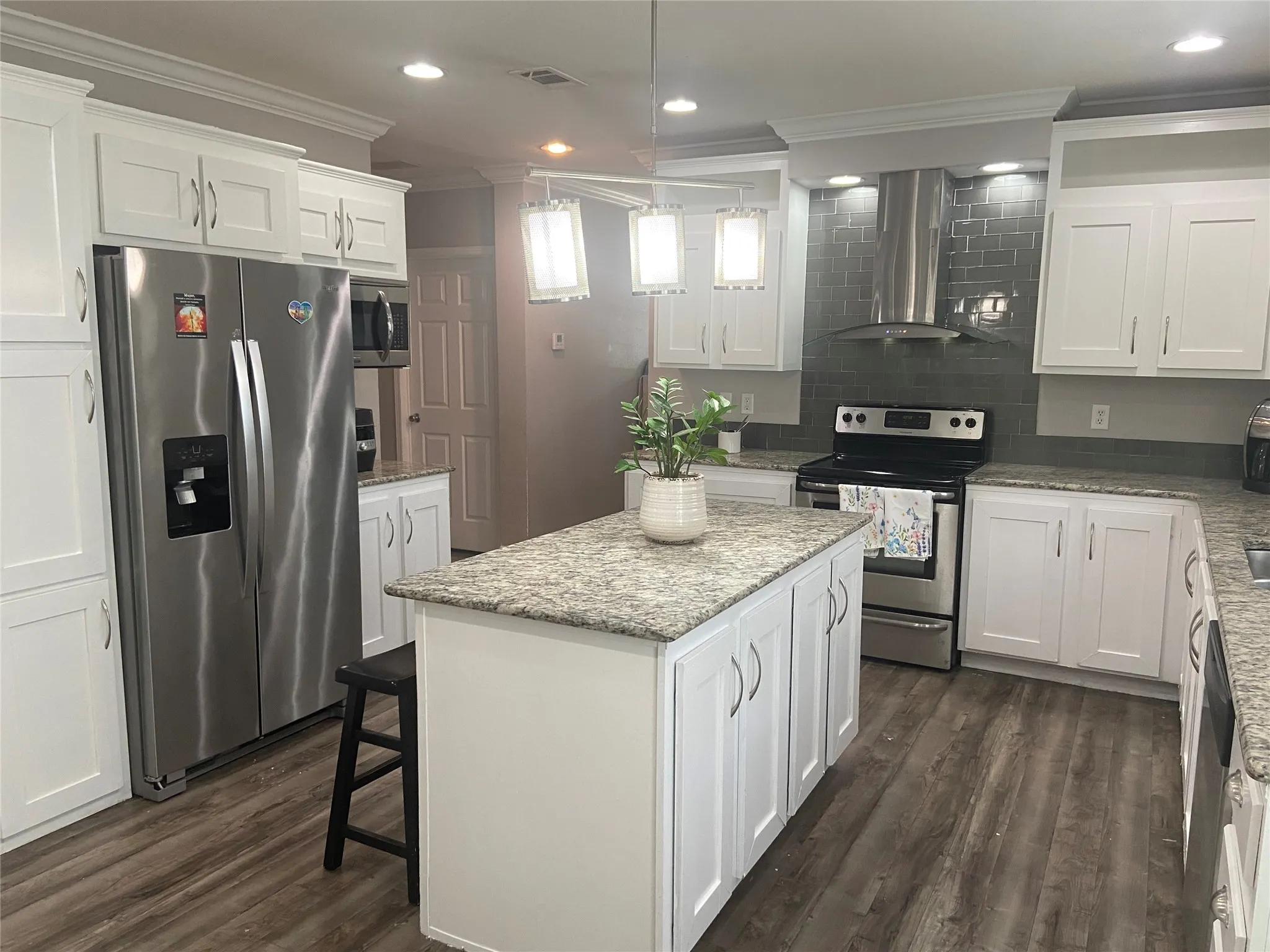 Kitchen featuring white cabinets, stainless steel appliances, crown molding, a kitchen island, and wall chimney range hood