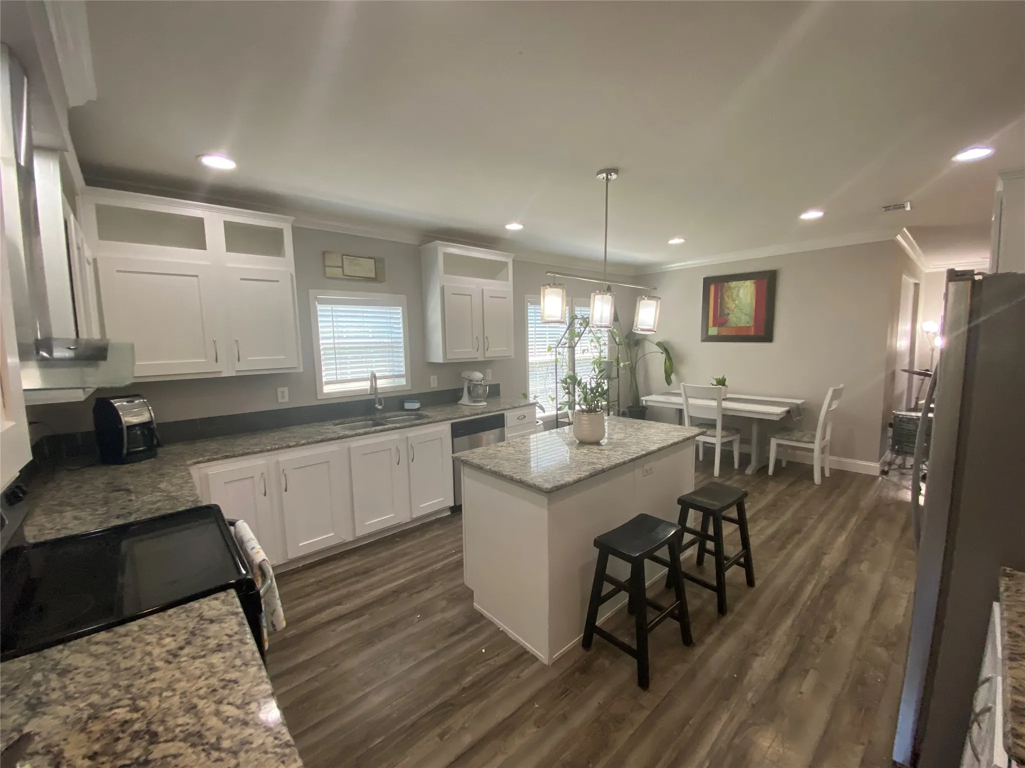 Kitchen with a breakfast bar area, glass insert cabinets, white cabinetry, appliances with stainless steel finishes, and light stone countertops
