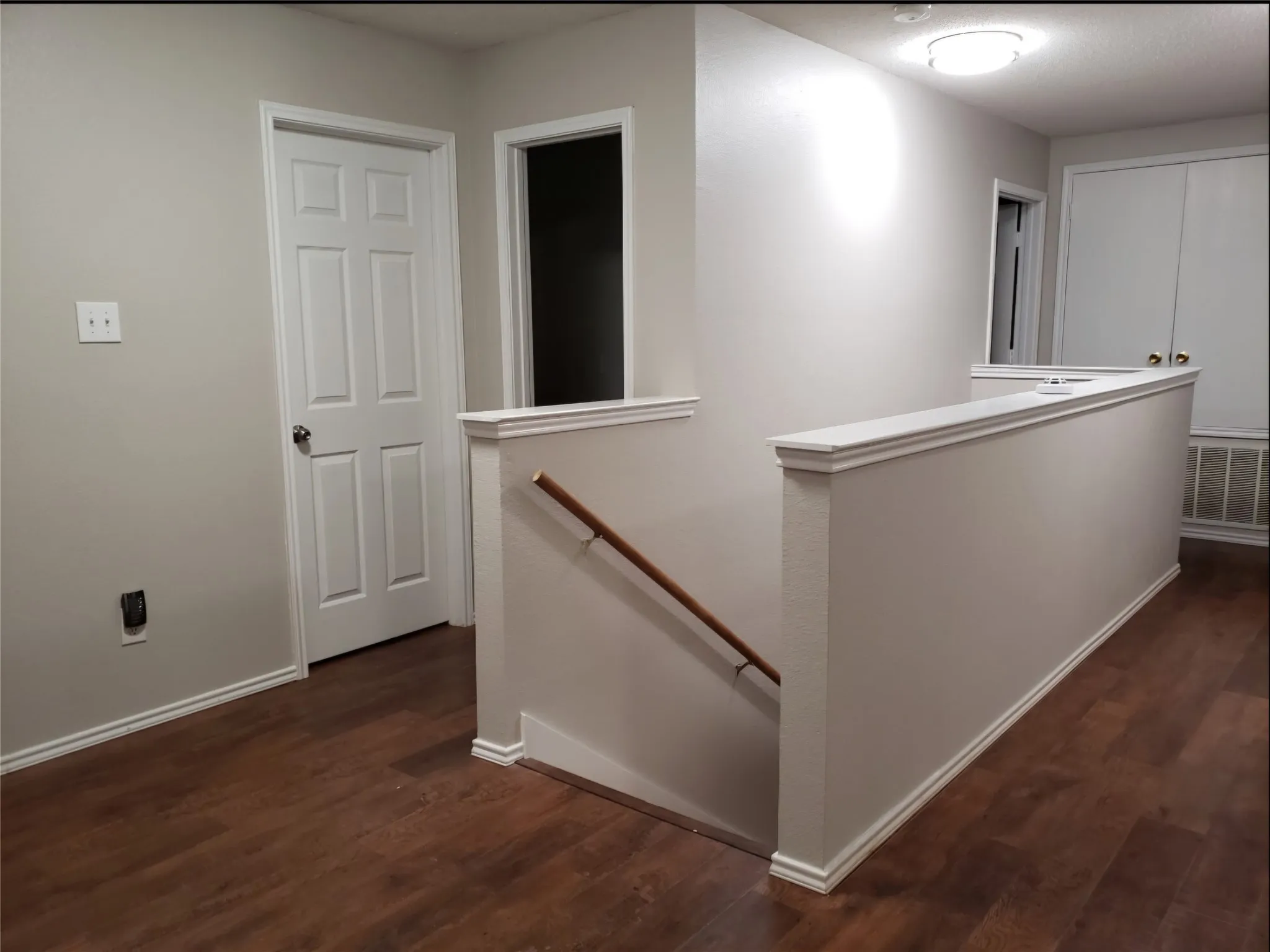 Wood-finish flooring, white trim, light-toned walls, six-panel interior door, and a built-in handrail