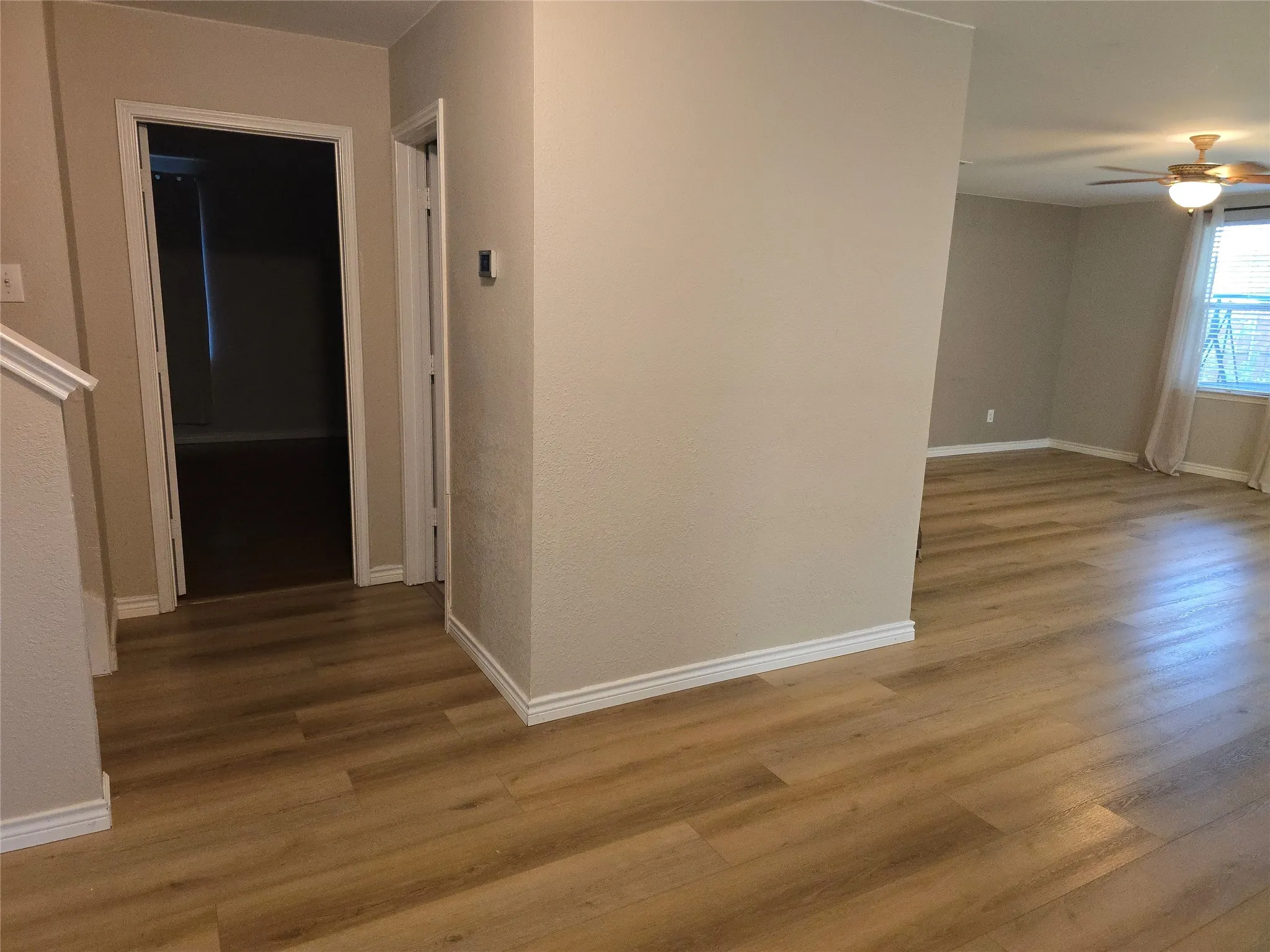 Wood-finish flooring throughout, neutral painted walls, white trim, and a ceiling fan with integrated lighting